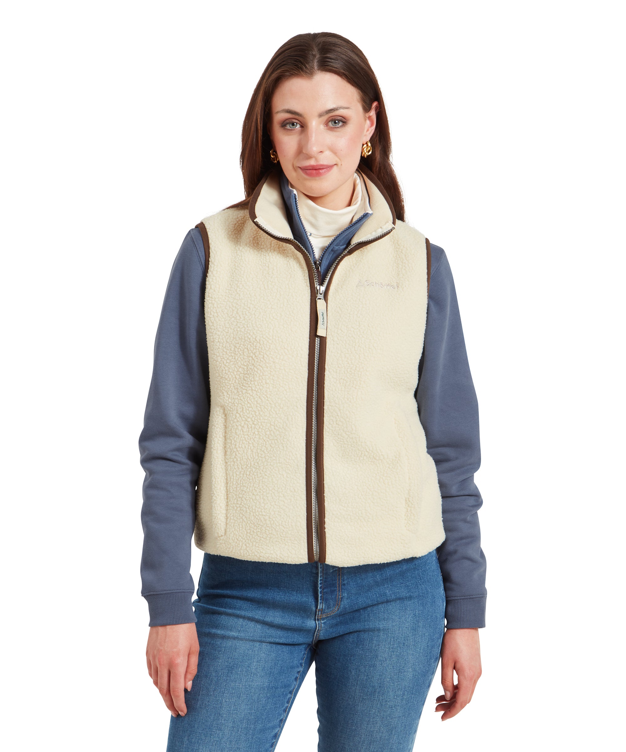 A woman is wearing a Schöffel Lyndon Retro Fleece Gilet for Women in Cream over a light blue long-sleeve top. She is standing with a relaxed expression, with her arms resting by her sides.