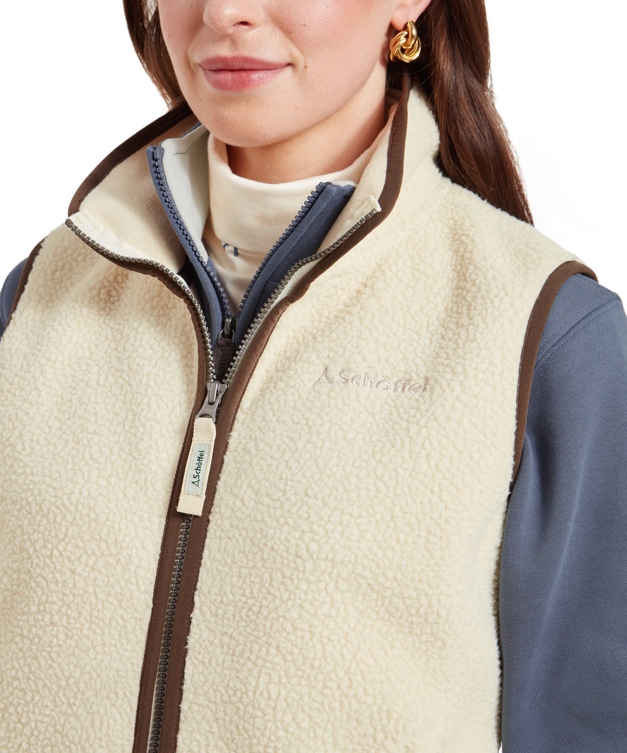 A close-up of the Schöffel Lyndon Retro Fleece Gilet for Women in Cream's zip, showing the brand label on the zip pull, along with the fleece's texture and the brown trim along the edges.