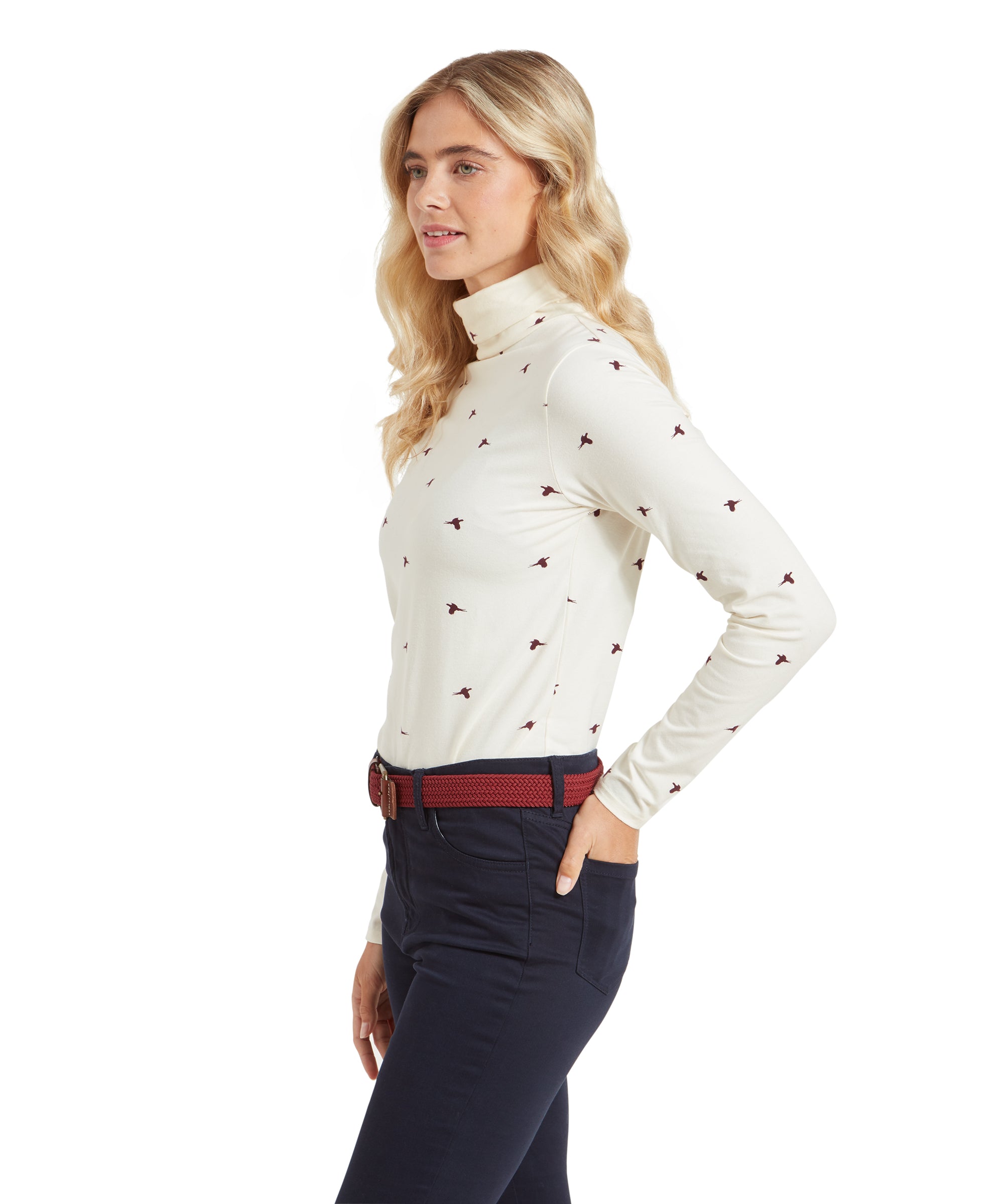 A woman in a profile view, wearing a Schöffel Malham Top for Women in Red with maroon bird prints, paired with dark navy pants and a red belt. She is looking slightly forward.