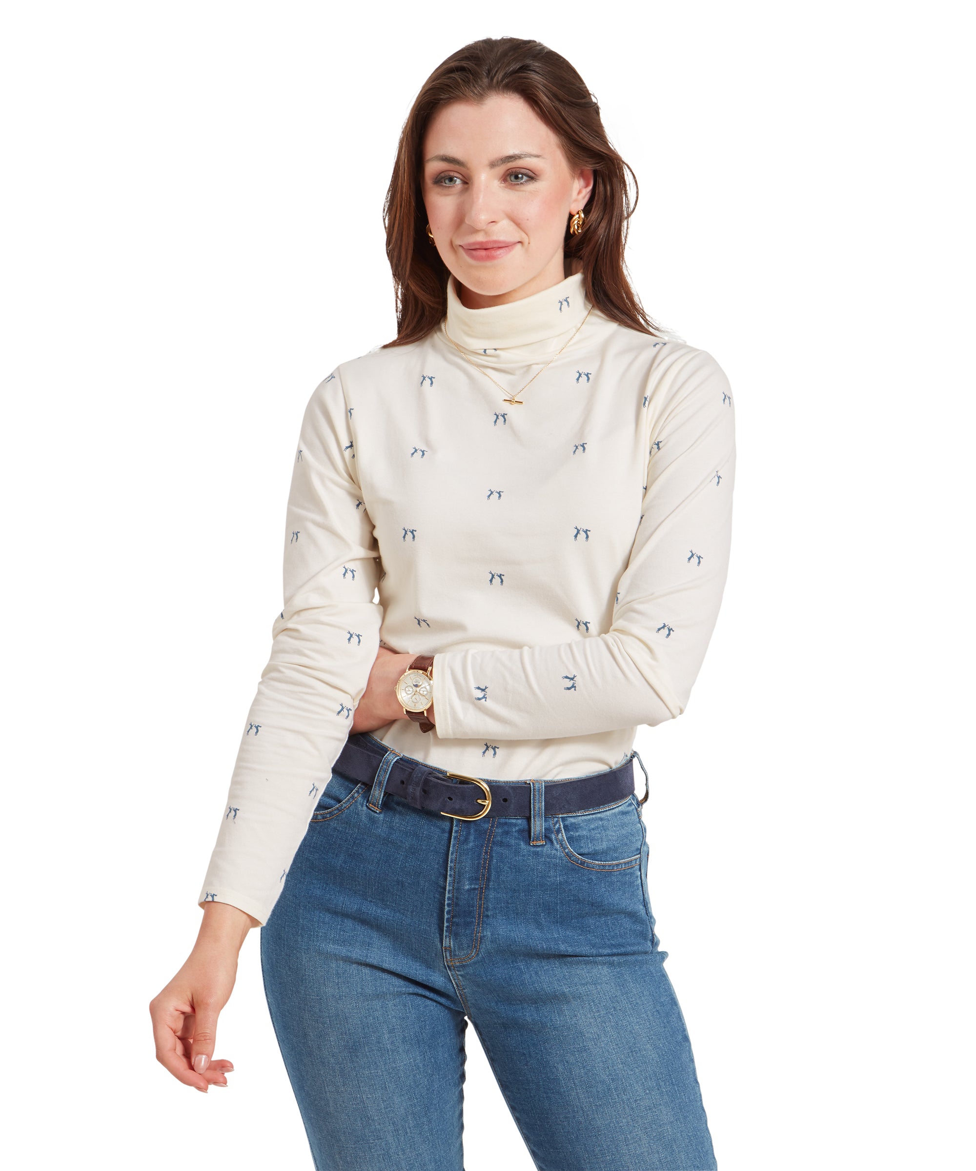 A woman wearing a Schöffel Malham Top for Women in Blue with a small blue pattern, paired with light blue jeans and a navy belt, standing with her arms crossed, smiling softly.