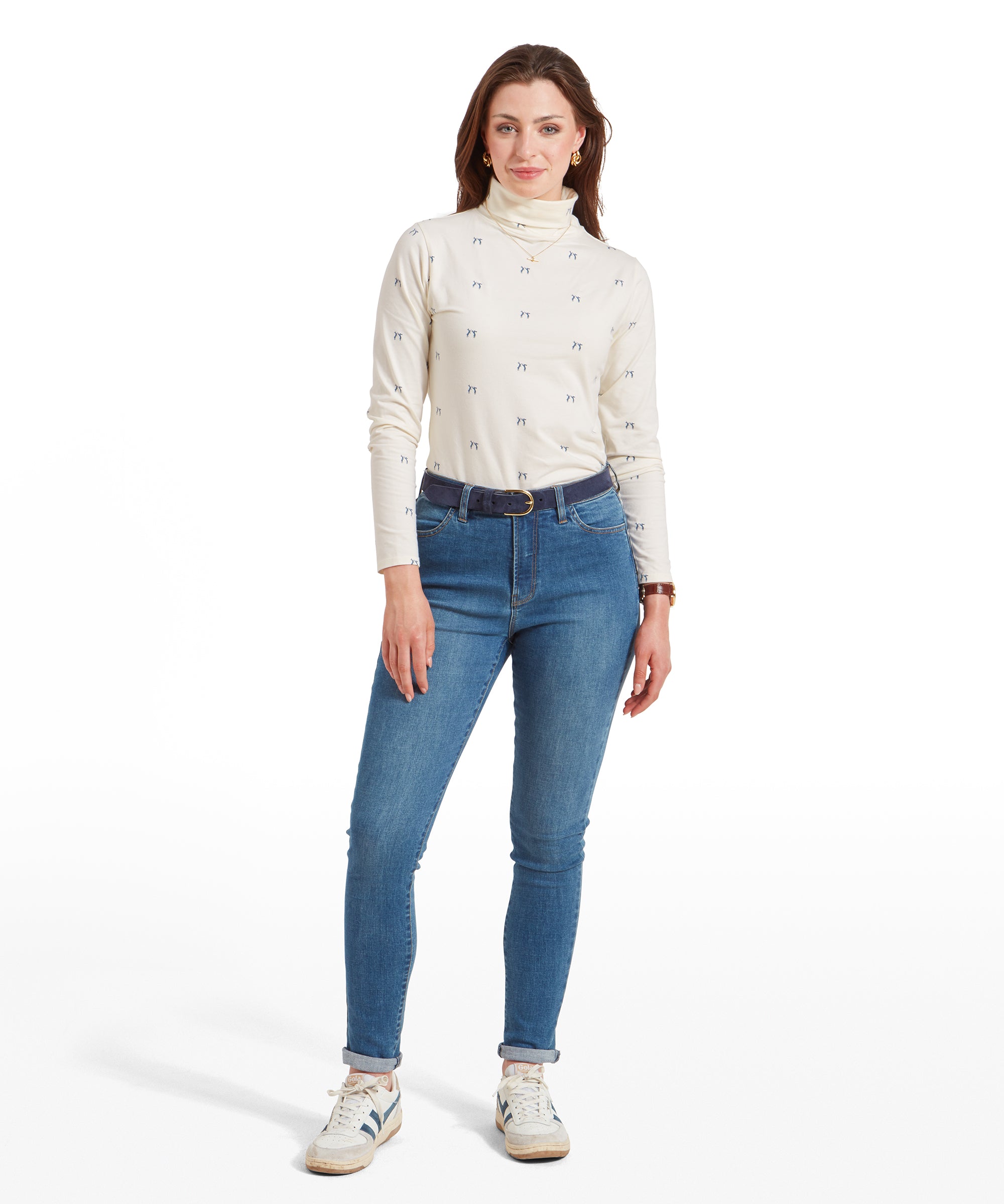 A full-body shot of a woman in a Schöffel Malham Top for Women in Blue with a small blue pattern, paired with light blue jeans and white trainers, standing with her left hand in her pocket.