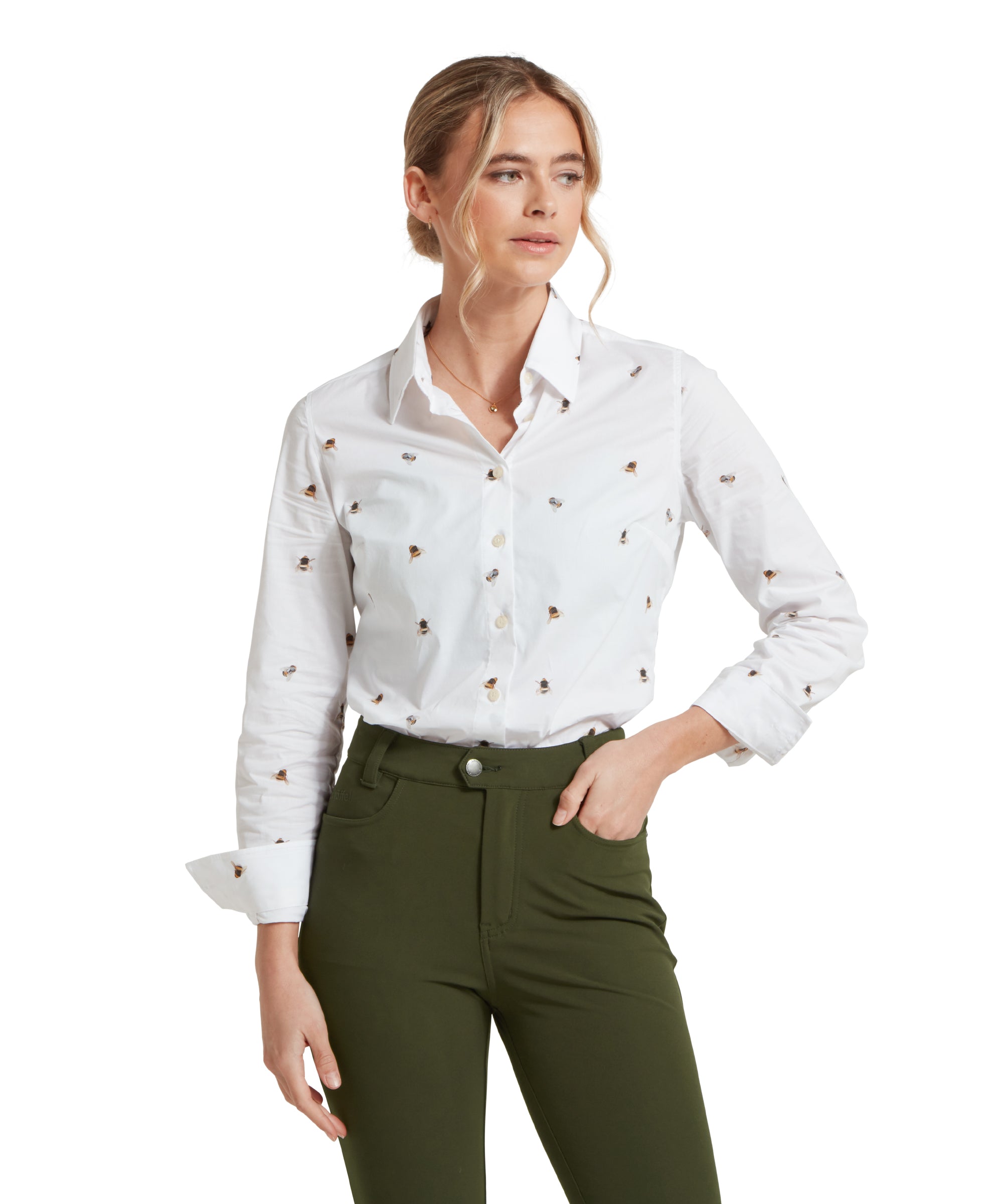 Close-up of a female model wearing a white Schöffel shirt with a bee pattern, paired with mid green trousers. Model is standing in a relaxed pose with one hand in her pocket and cuffs rolled up.