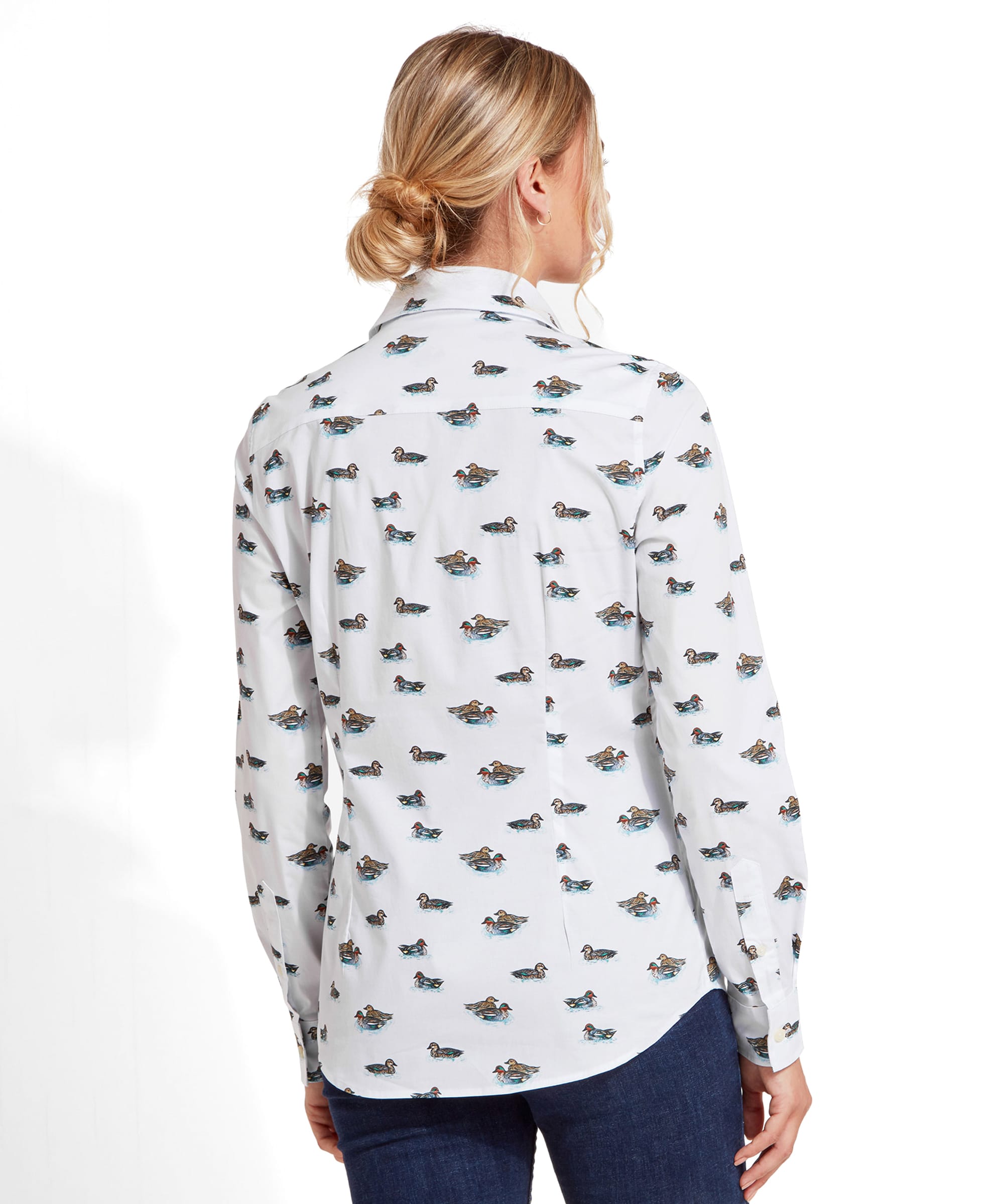 A back view of the woman wearing the Schöffel Norfolk Shirt for Womens in Blue with duck prints. Her blonde hair is tied into a low bun, and she is wearing dark jeans.