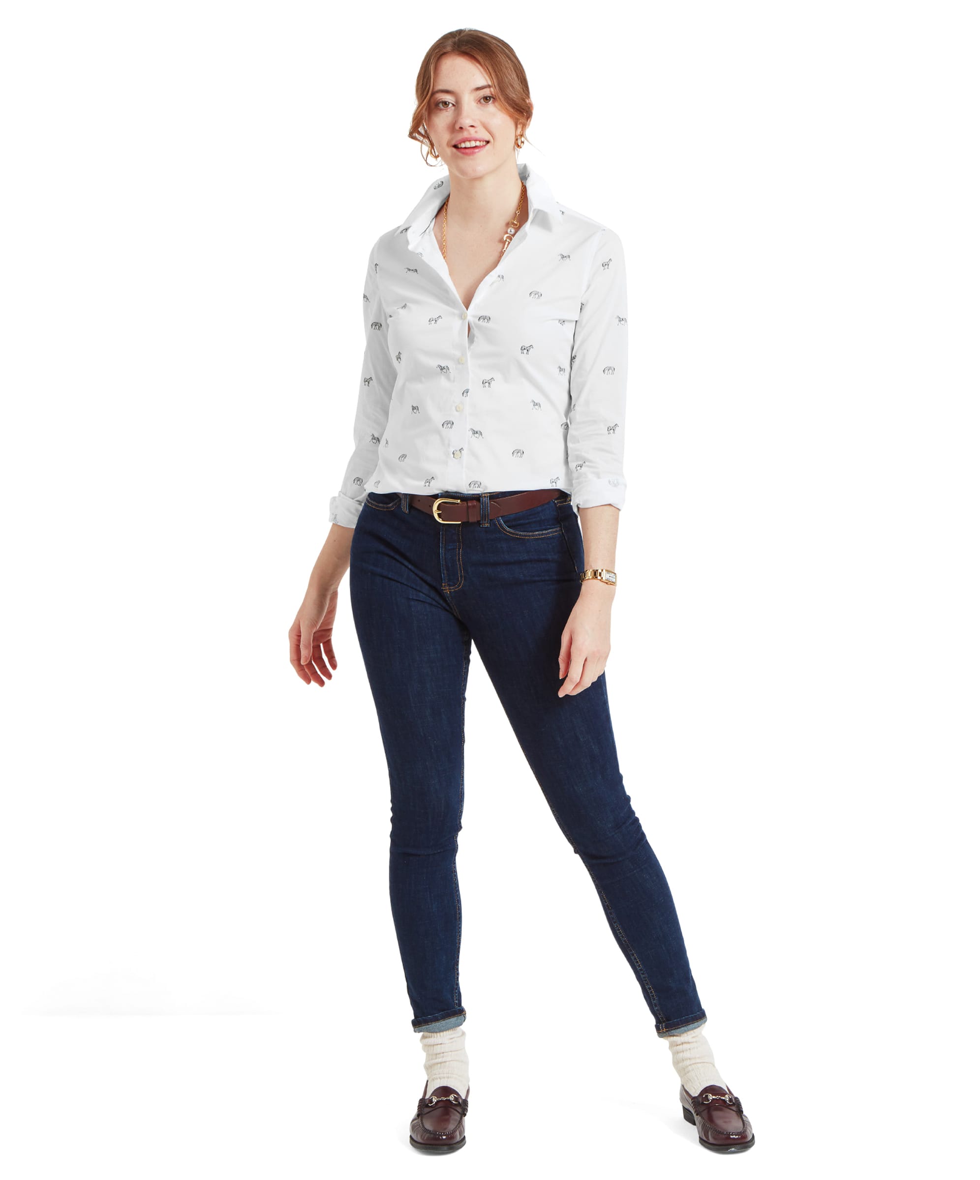 The same woman is standing in a full-body shot, showing the full outfit with the Schöffel Norfolk Shirt for Womens in White Black, blue jeans, and brown belt. She is wearing brown loafers and light-colored socks, and her expression is relaxed and content.