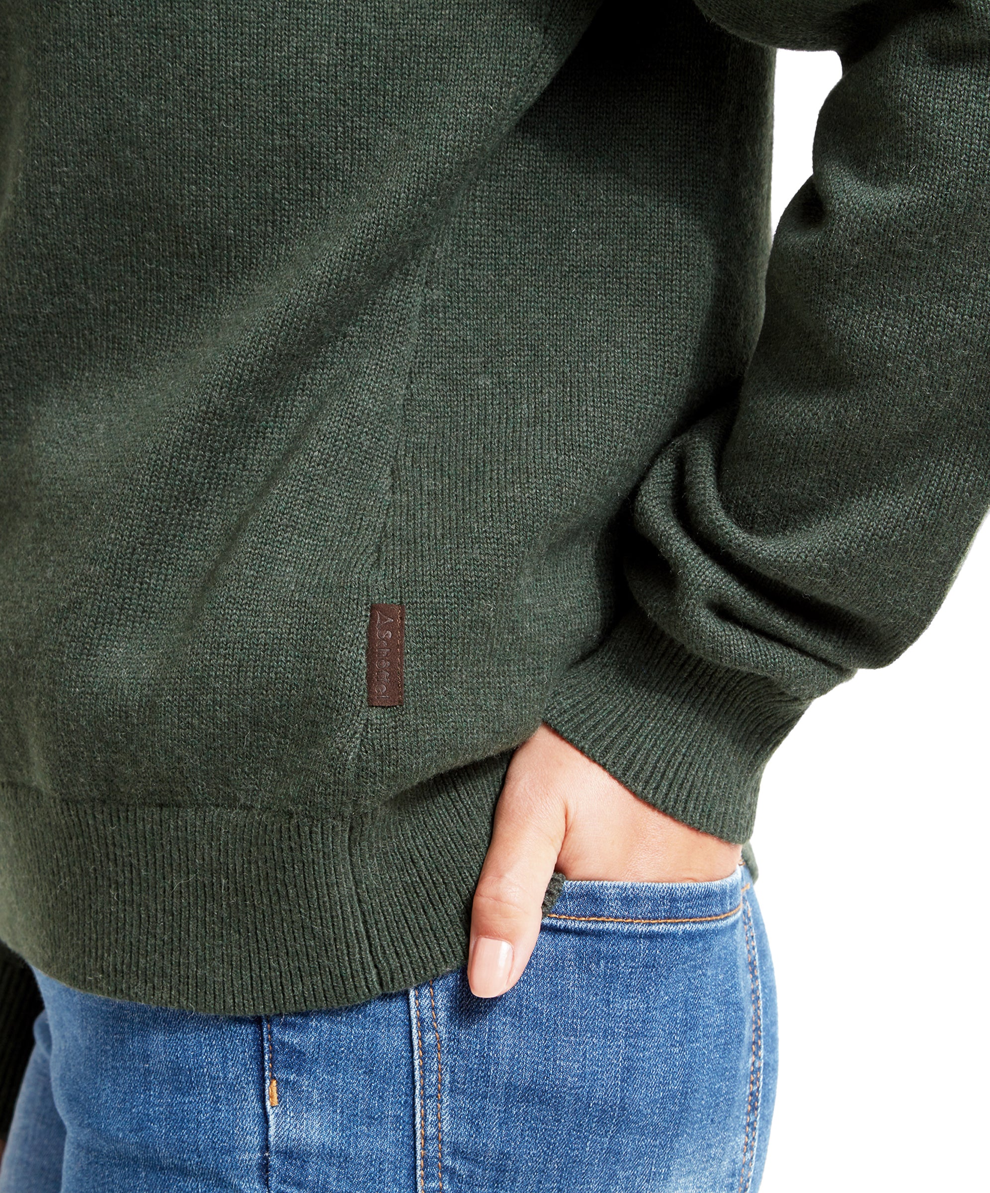 A close-up of the woman's side, showing the bottom of the Schöffel Pateley Jumper for Women in Green and the top of her blue jeans. A small leather tag with "Schöffel" branding is visible on the jumper.