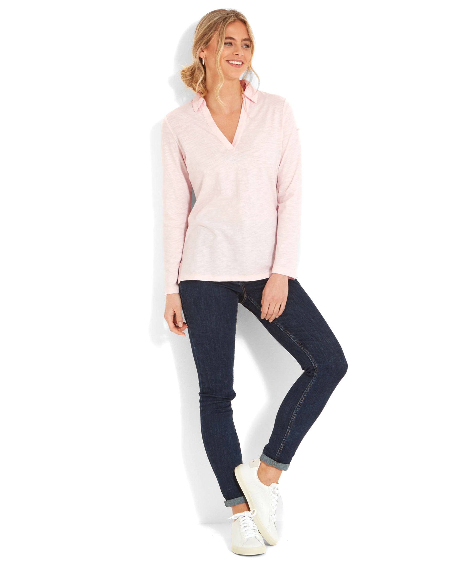 The same woman standing and wearing the Schöffel Pentle Bay Top for Women in Pink paired with dark jeans and white sneakers. She is leaning slightly against a white wall.