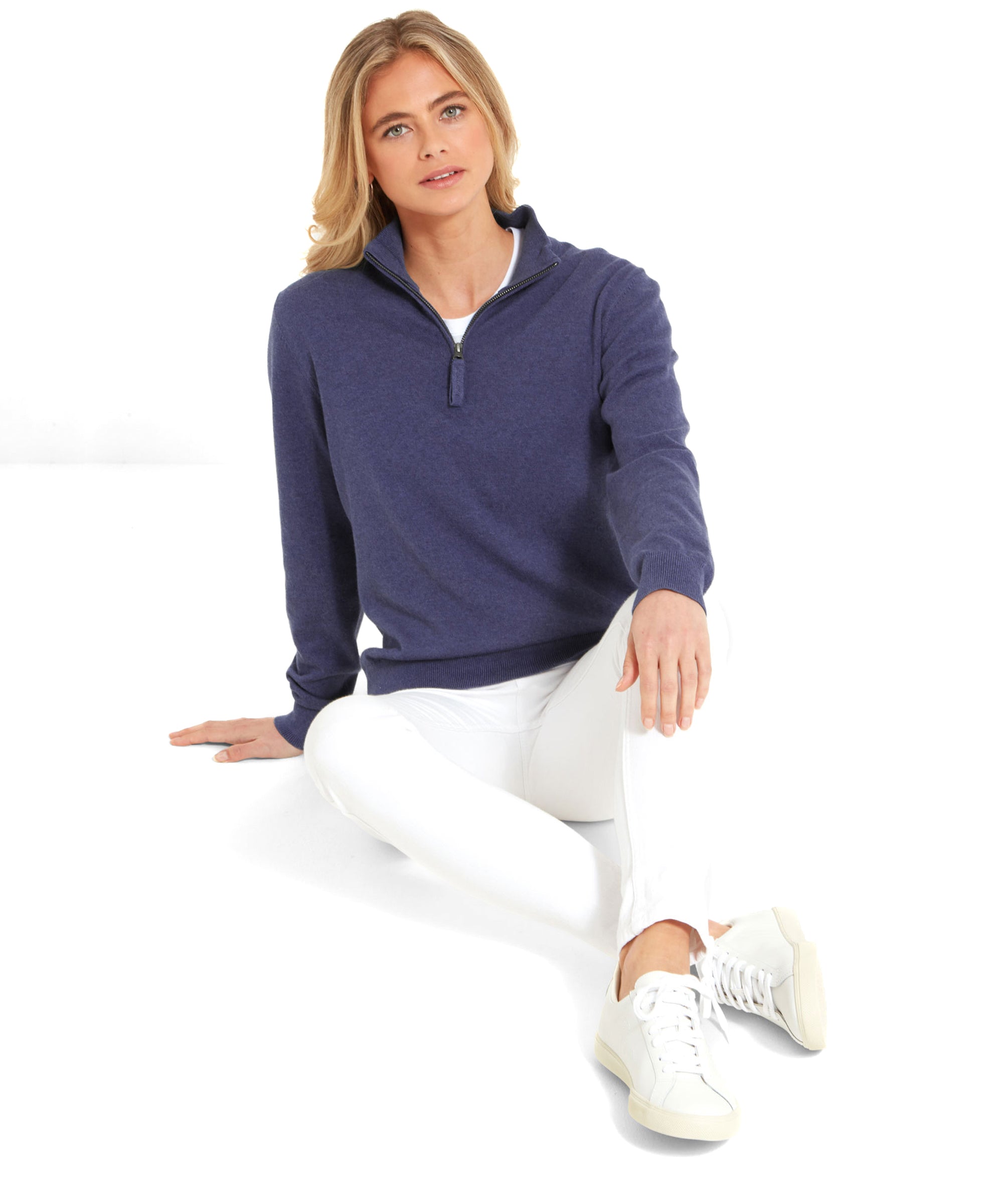 Full-body image of a woman sitting on the floor wearing a Schöffel Polperro Pima Cotton 1/4 Zip for Women in Navy Blue and white trousers.