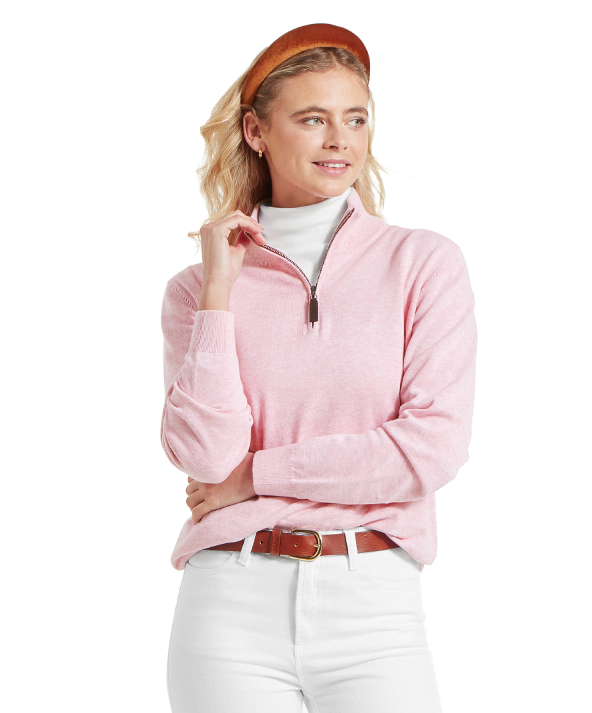 Woman wearing a Schöffel Polperro Pima Cotton 1/4 Zip for Women in Pale Pink over a white turtleneck, accessorised with a brown headband, white jeans, and a brown belt, gazing to the side.