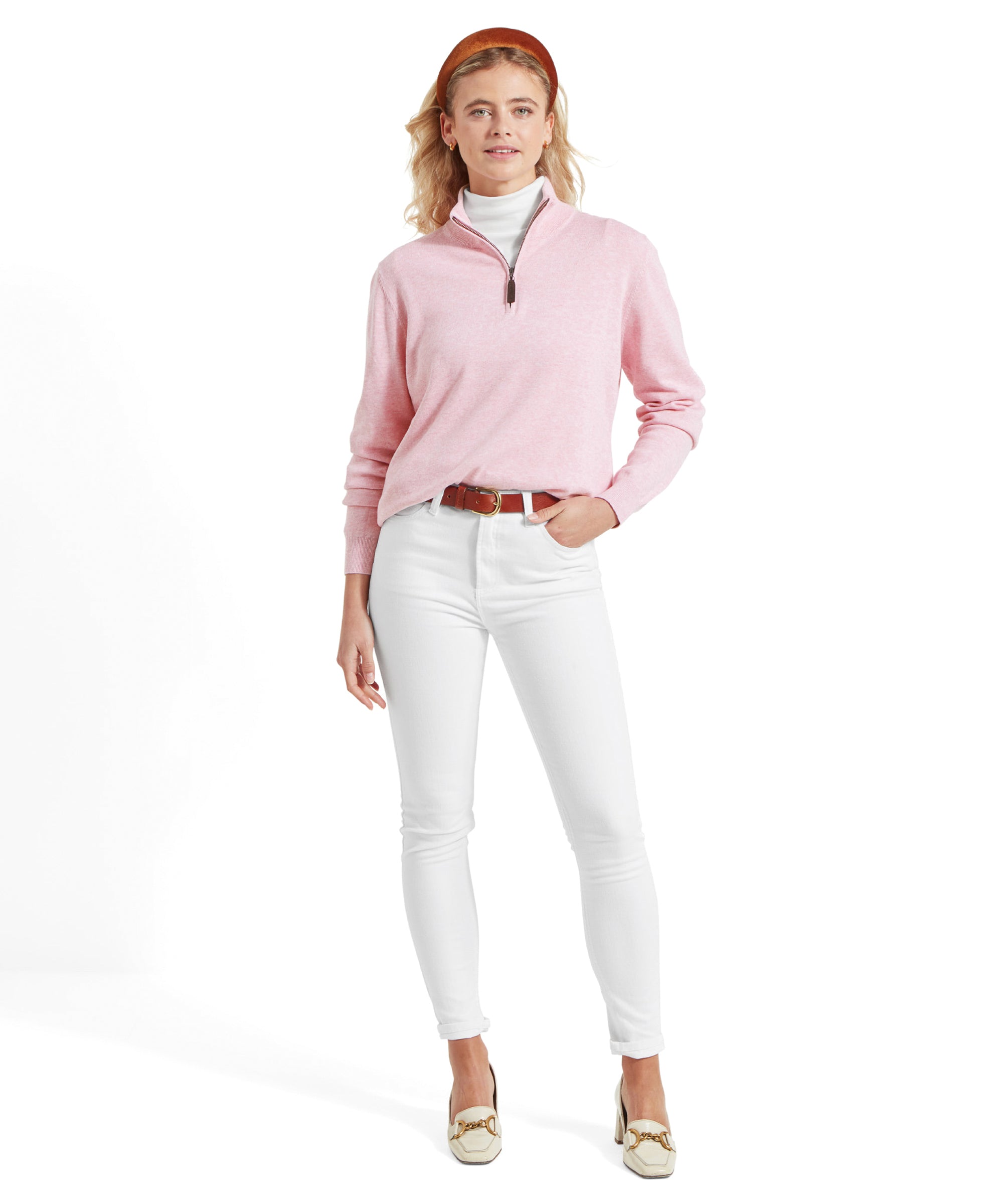 Full-body view of the woman in the Schöffel Polperro Pima Cotton 1/4 Zip for Women in Pale Pink, white jeans, and brown belt, standing with a confident pose and one hand in her pocket.