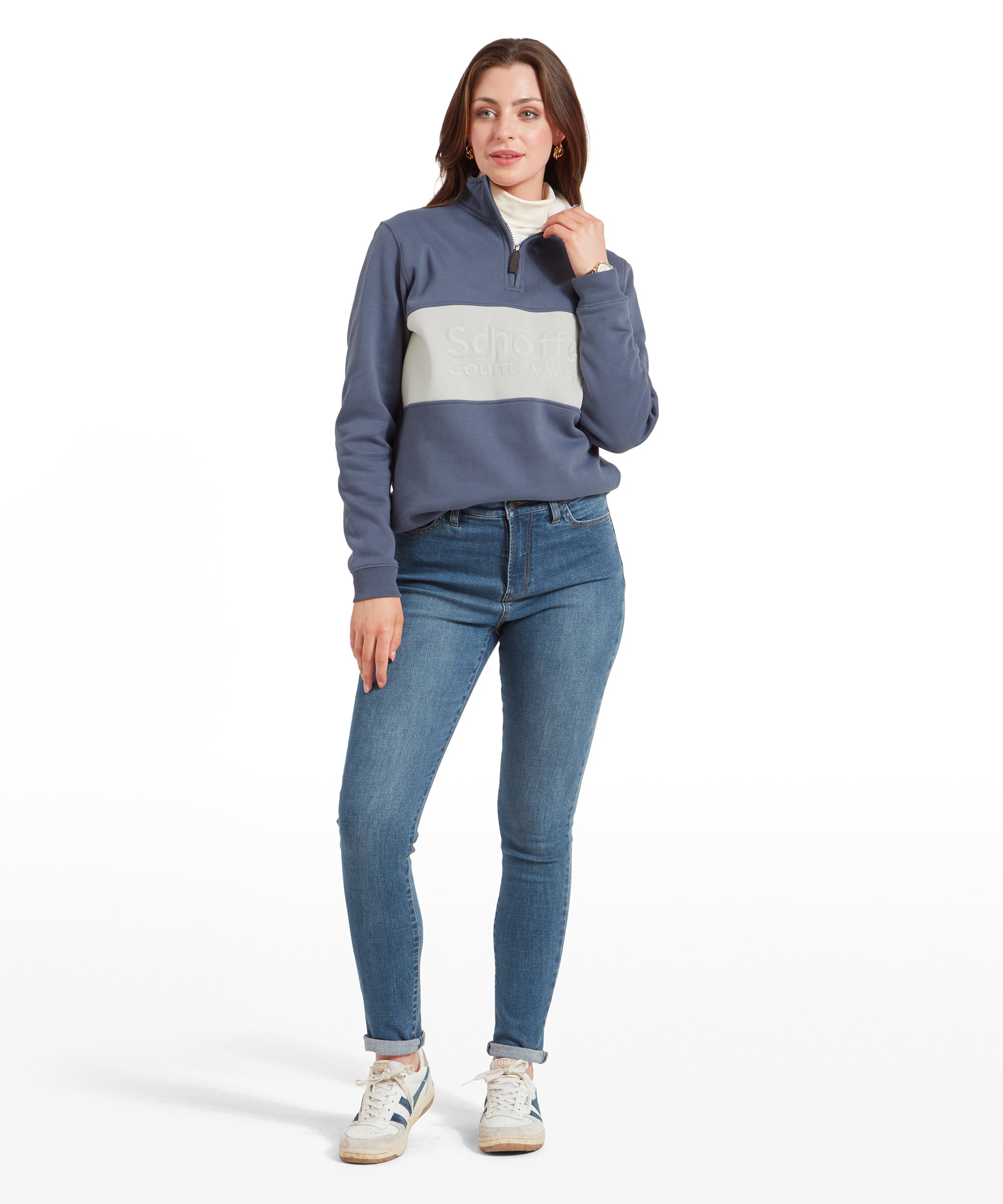 Full-body view of a woman wearing Schöffel Poppy Jean for Womens in Blue, a blue and white striped sweatshirt, and white trainers, standing with one hand touching her collar.