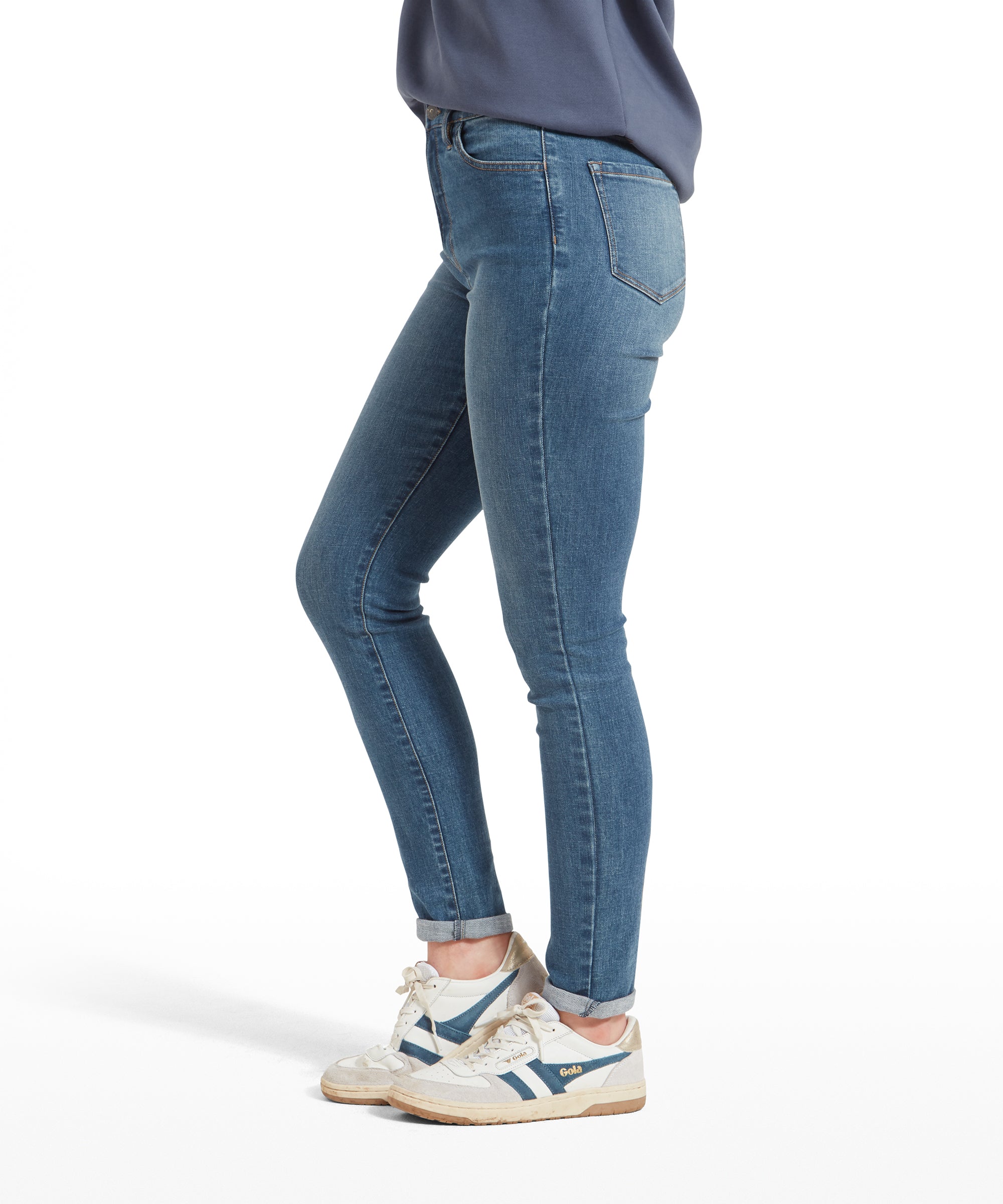 Side view of a woman wearing Schöffel Poppy Jean for Womens in Blue, a blue and white striped sweatshirt, and white trainers, showing the slim fit of the jeans.