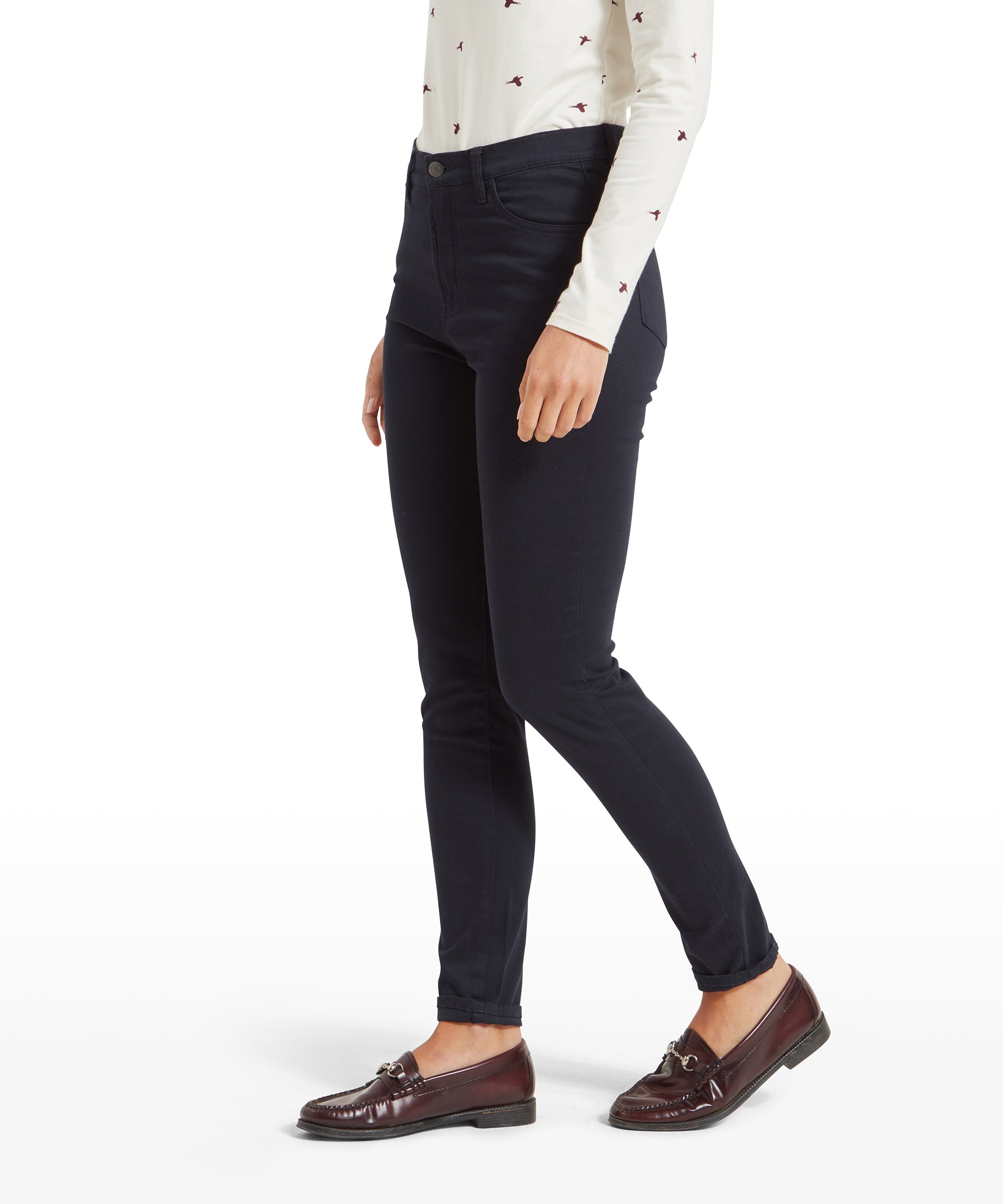 Side view of a woman wearing Schöffel Poppy Jean for Womens in Navy with a high waist, paired with a cream-colored long-sleeved top featuring small red bird motifs, showing the fit of the jeans along the leg.