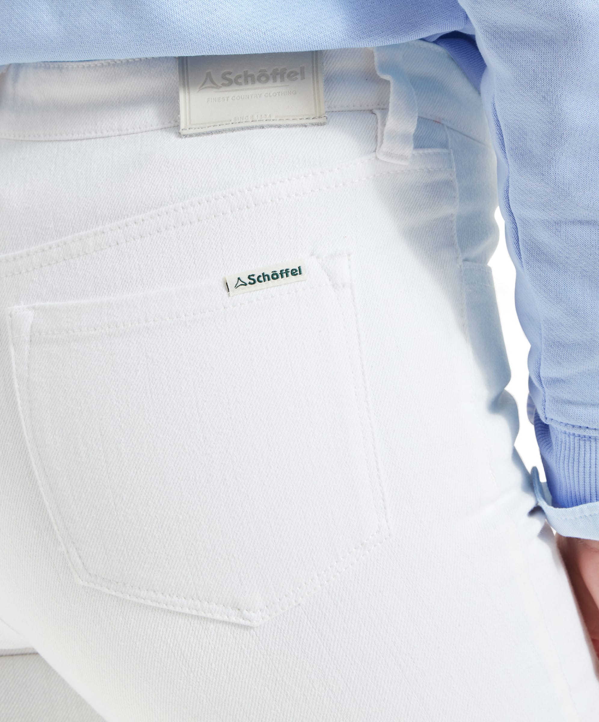 Close-up of the back pocket and waistband of Schöffel Poppy Jean for Womens in White. The pocket has a small fabric tag with the brand "Schöffel" and a leather patch on the waistband with the same branding.