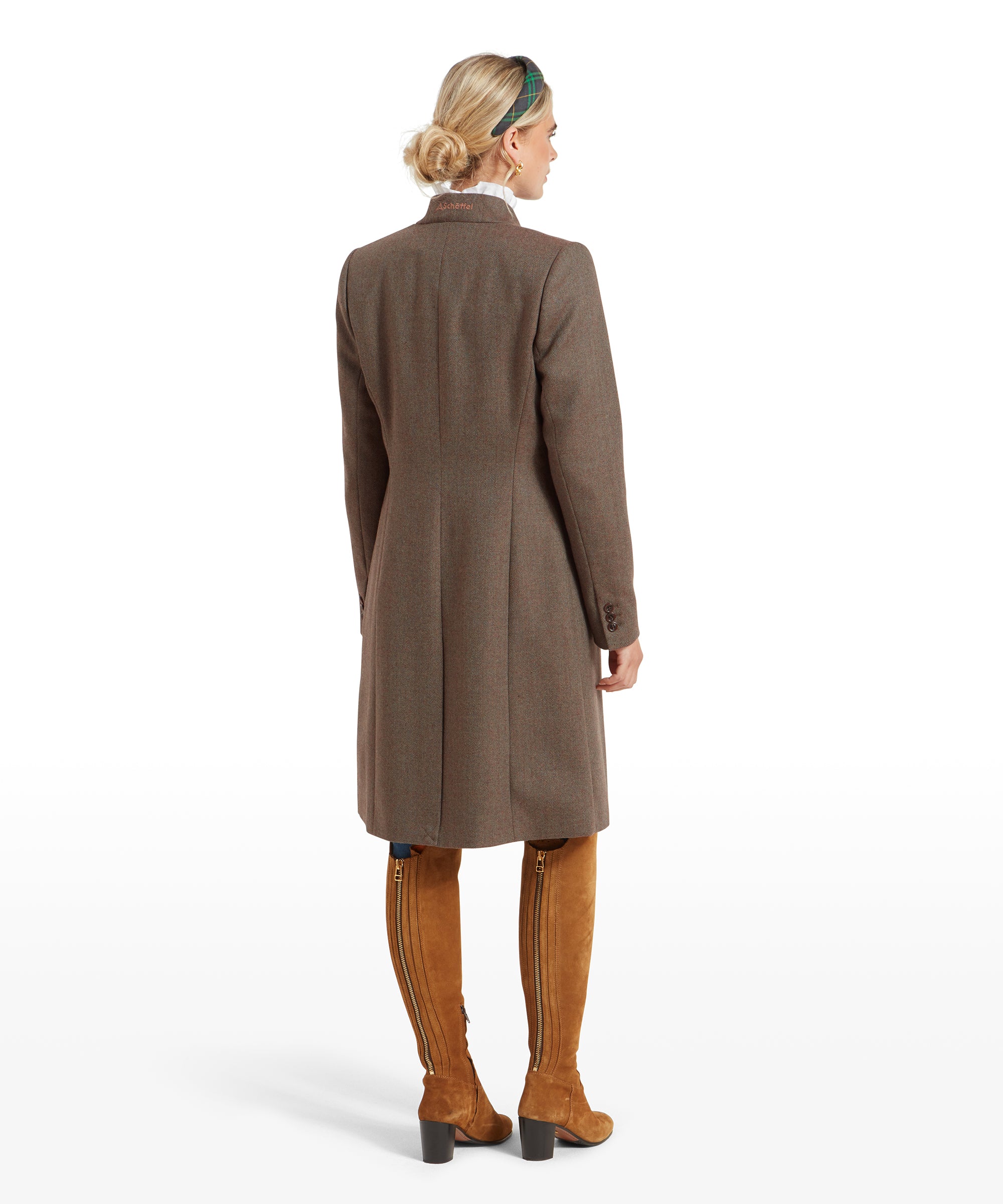 Rear view of a woman in a Schöffel Portree Tweed Jacket for Women in Green, tan knee-high boots, and a green headband. The coat's back detailing is visible.