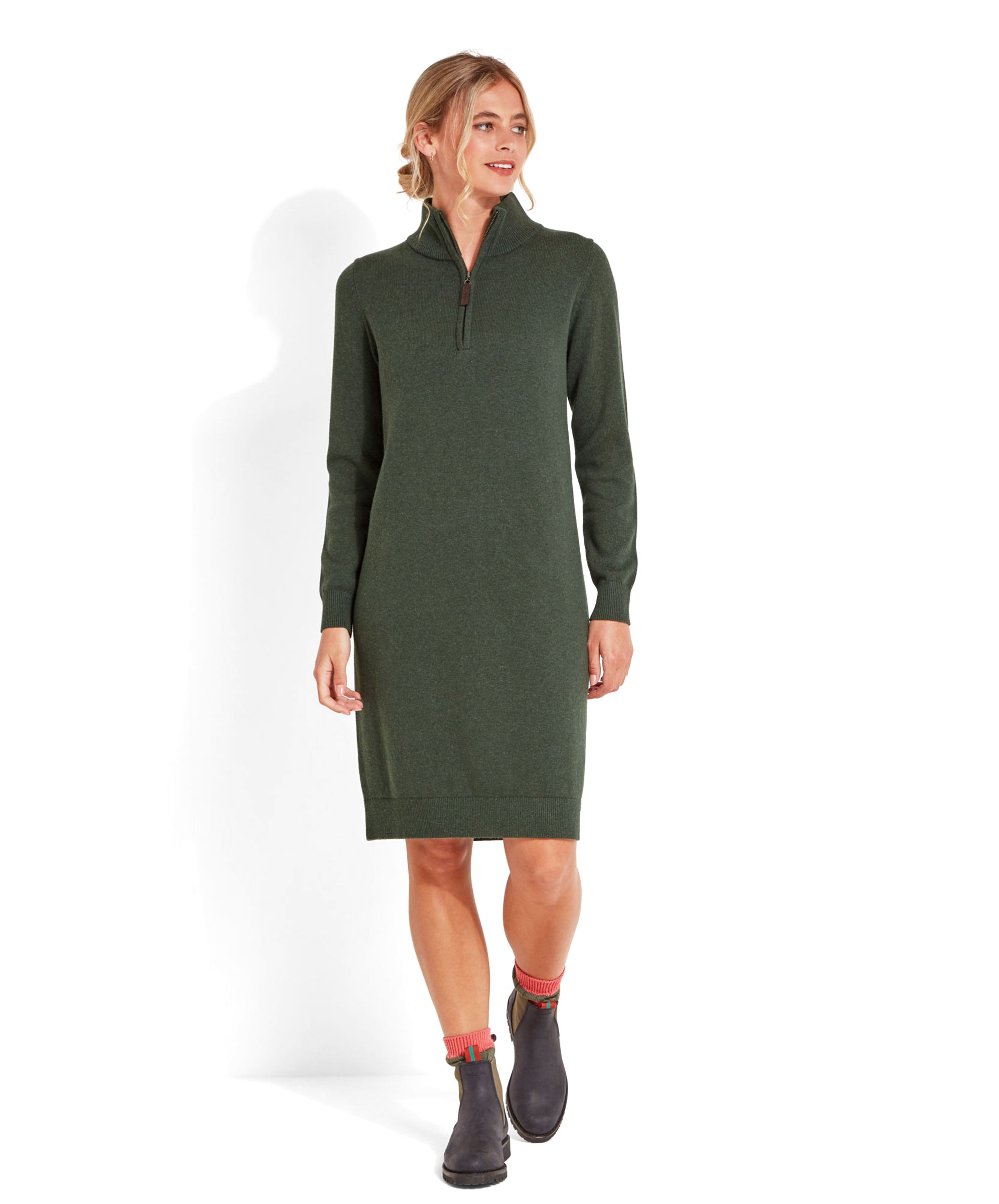 A blonde woman models a Schöffel Primrose Dress for Women in Green with a quarter-zip neckline, styled with navy ankle boots and pink socks.