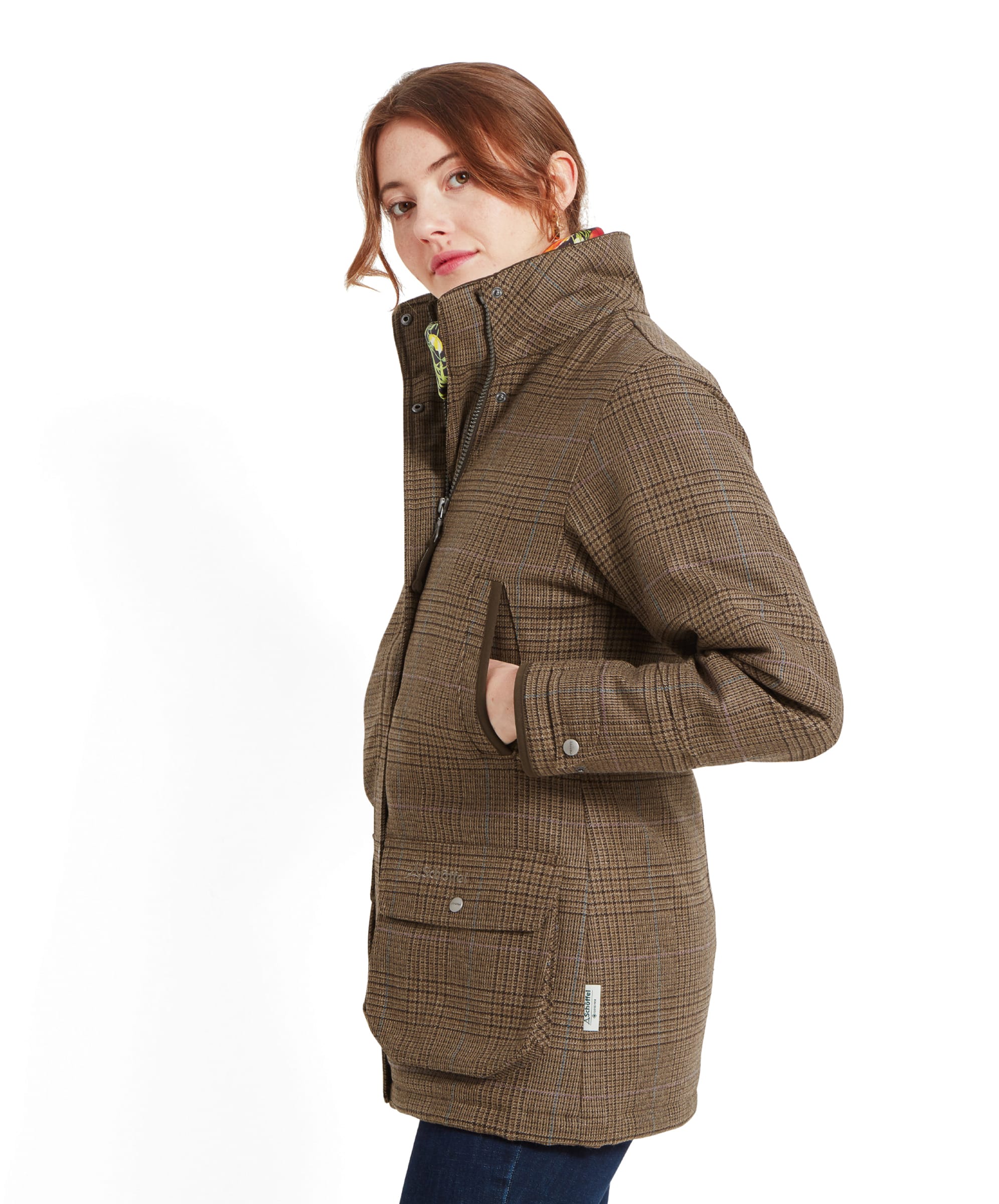 Side view of a woman wearing a Schöffel Ptarmigan Tweed Coat for Women in Brown. She is looking over her shoulder with her left hand in the coat pocket, highlighting the coat's tailored fit and classic design.