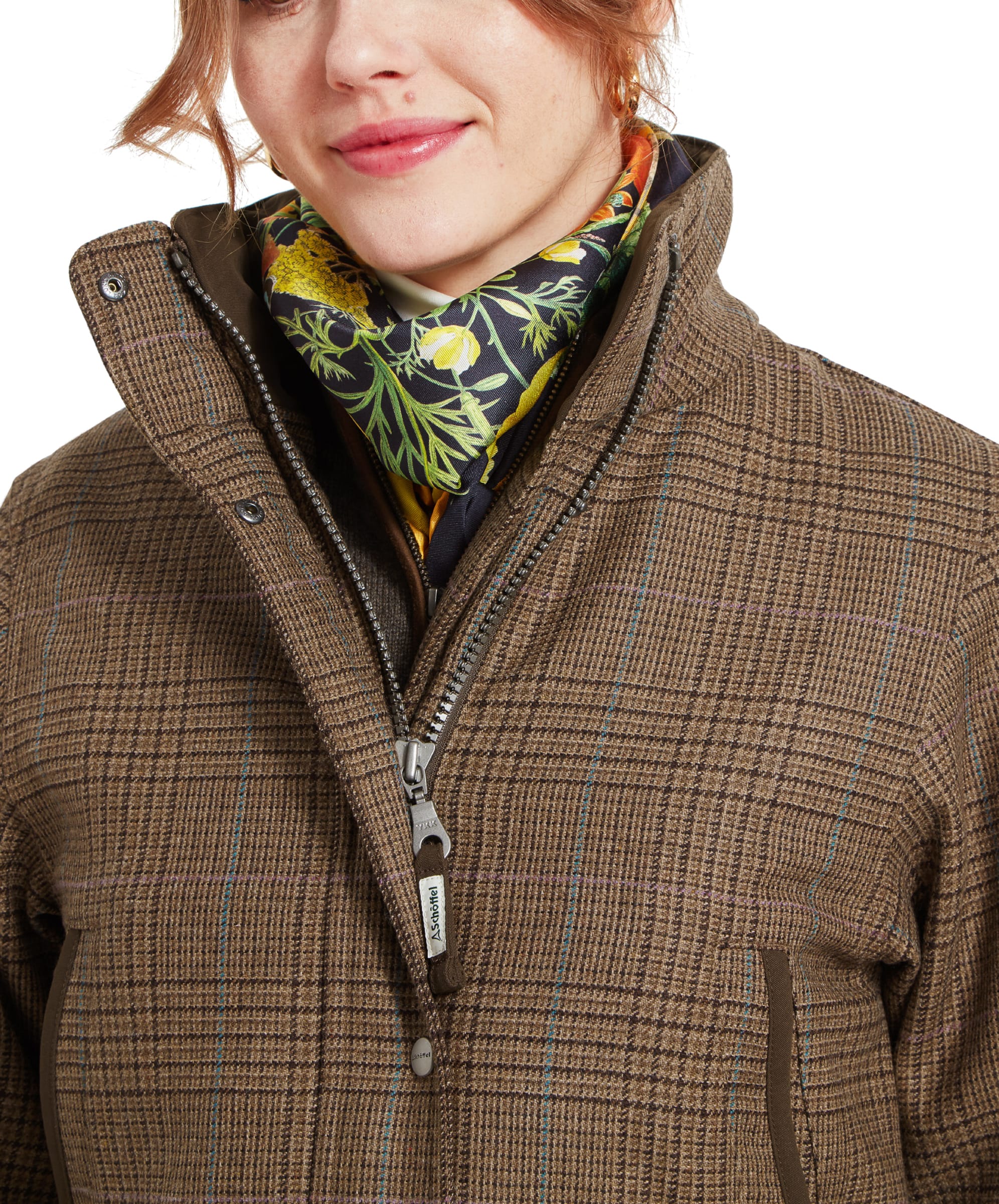 Close-up of the upper half of a woman wearing a Schöffel Ptarmigan Tweed Coat for Women in Brown with a high collar. She is smiling slightly and wearing a colorful floral scarf, adding a pop of colour to the outfit.