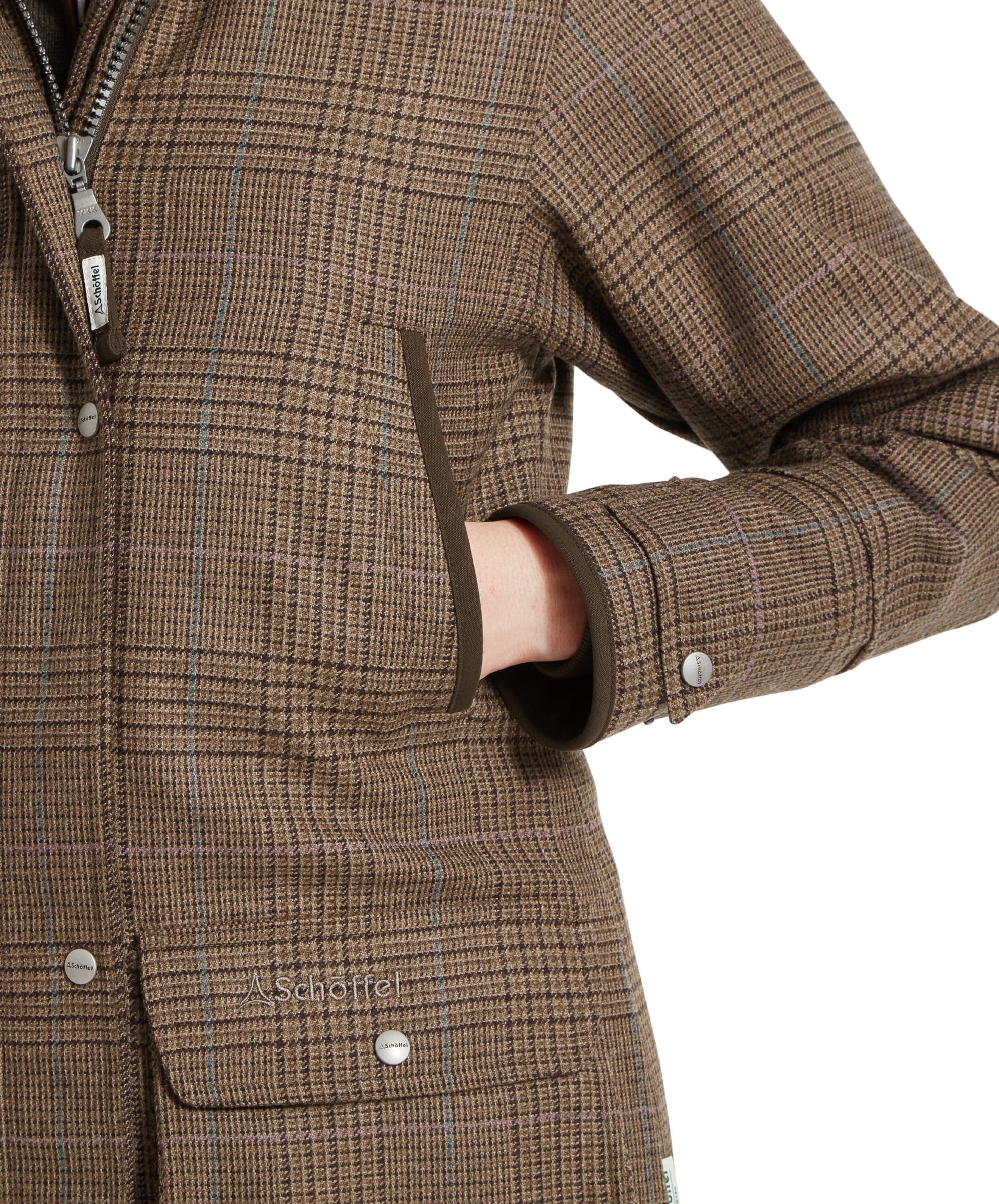 Detailed close-up of the front pocket of a Schöffel Ptarmigan Tweed Coat for Women in Brown. The pocket is accented with brown trim, and the woman’s hand is comfortably tucked into the pocket, emphasising the coat's practical design.