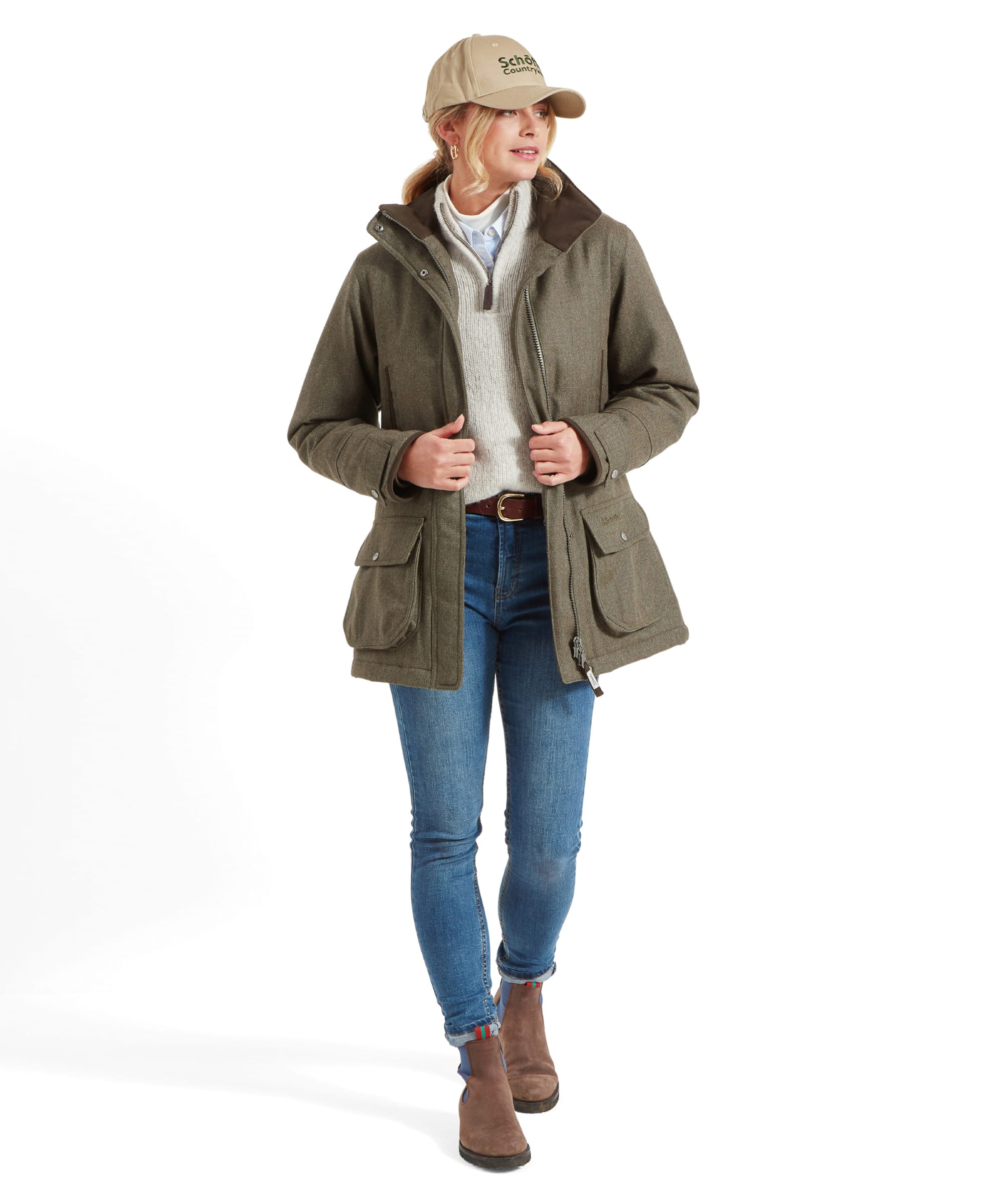 Full-body view of a woman wearing a Schöffel Ptarmigan Tweed Coat for Women in Green, beige sweater, blue jeans, and a beige baseball cap, standing with one foot slightly forward.