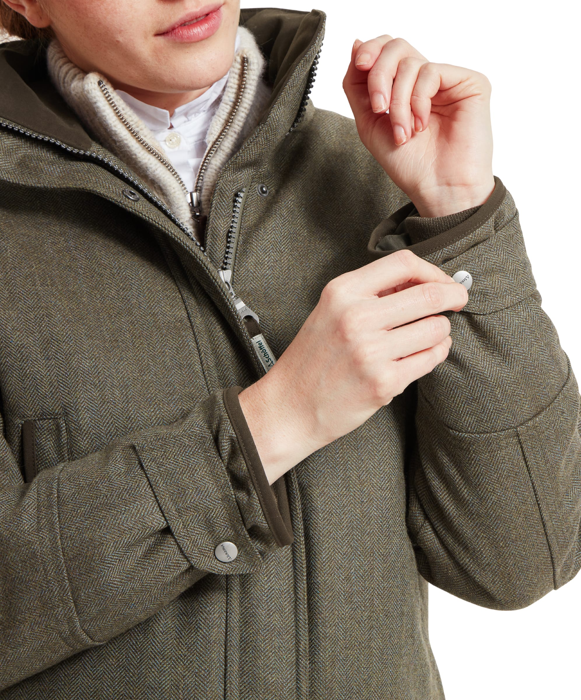 Close-up of a woman adjusting the cuff strap on the sleeve of a Schöffel Ptarmigan Tweed Coat for Women in Green, highlighting the coat's functional design.