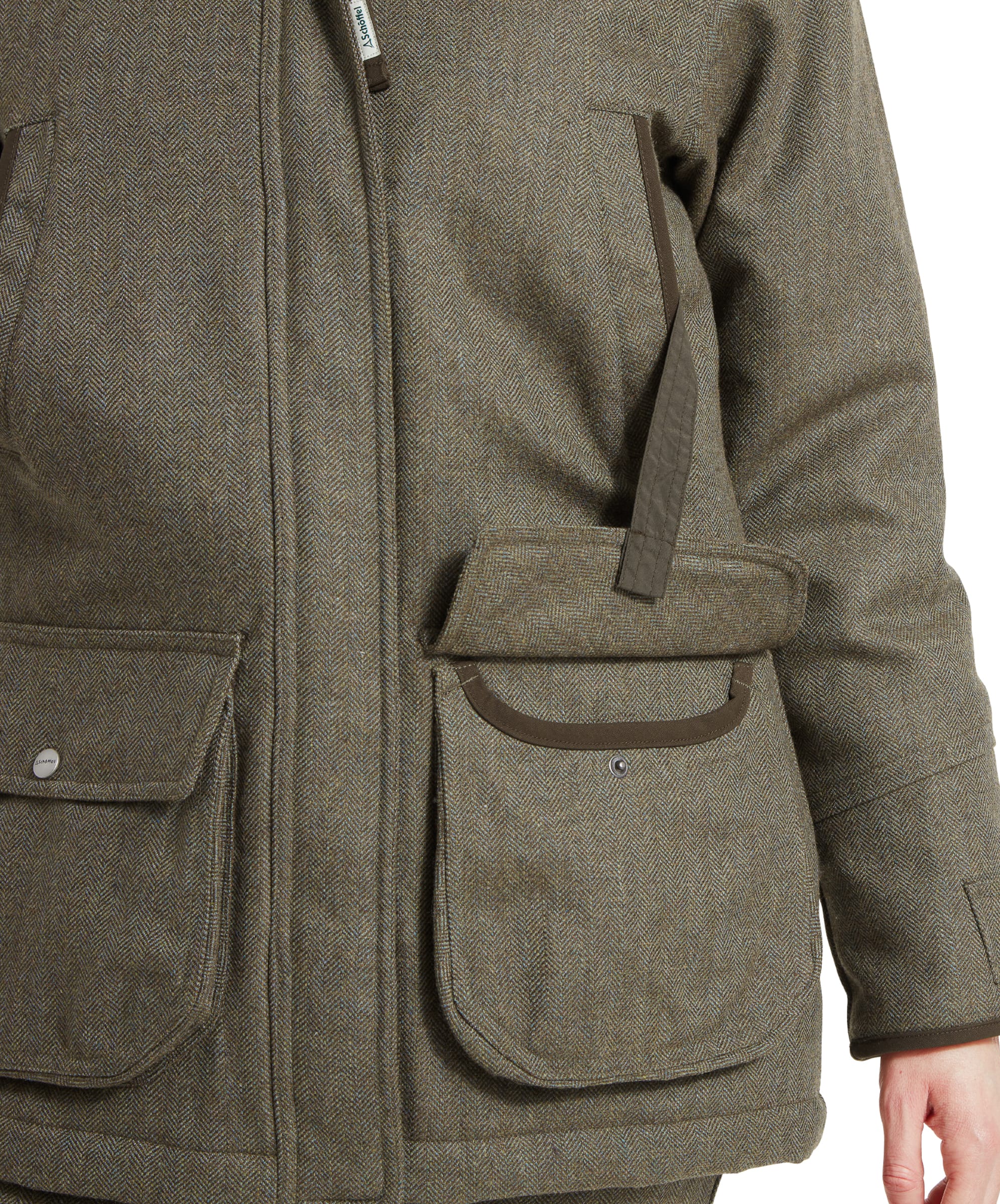 Close-up of the front pockets of a Schöffel Ptarmigan Tweed Coat for Women in Green, with one hand in the pocket, emphasising the practicality and detailing on the retainer strap.