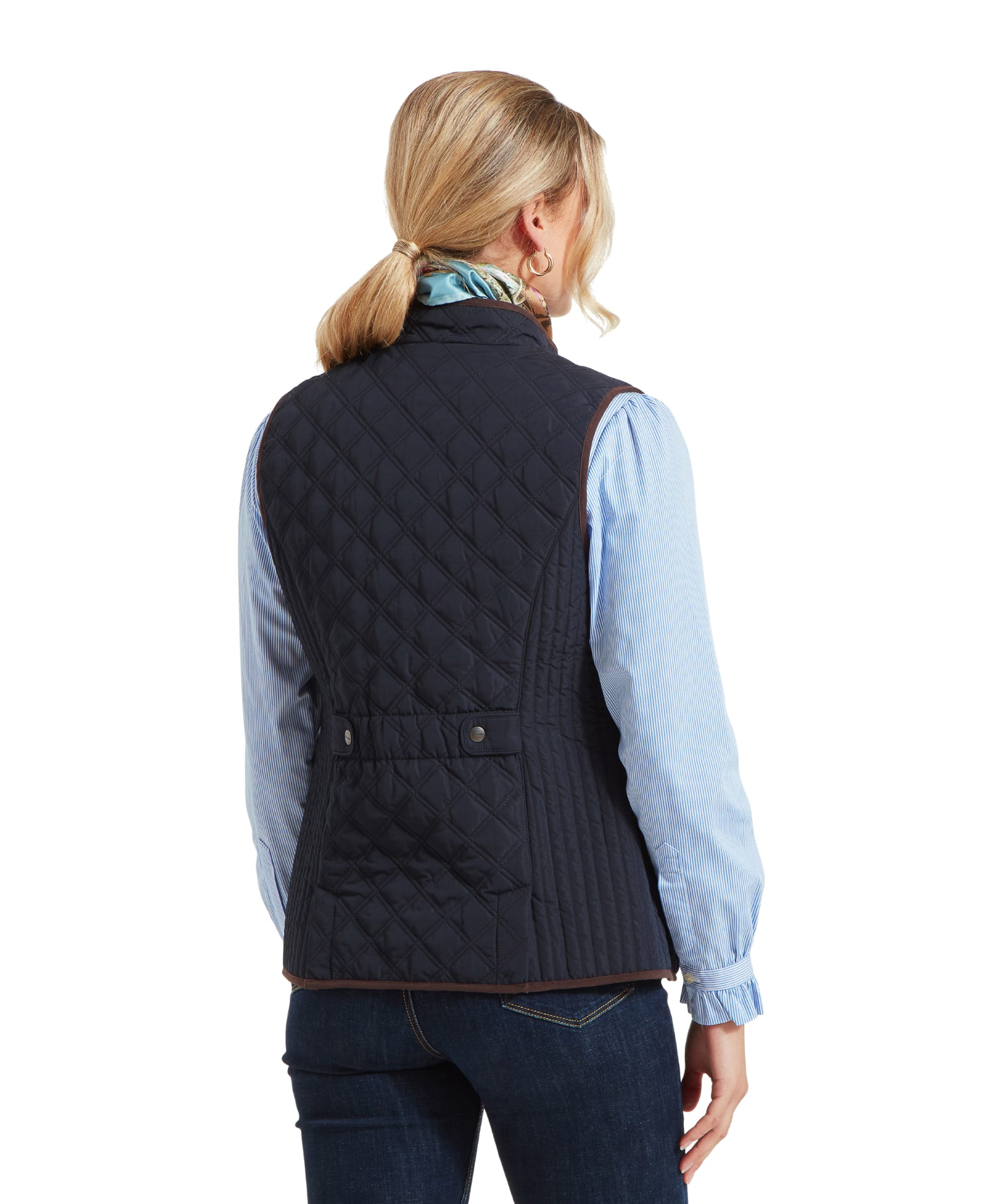 A rear view of a woman wearing a Schöffel Quilt Gilet for Women in Blue over a light blue shirt. The gilet features a cinched waist with buttoned side straps, adding a fitted look.