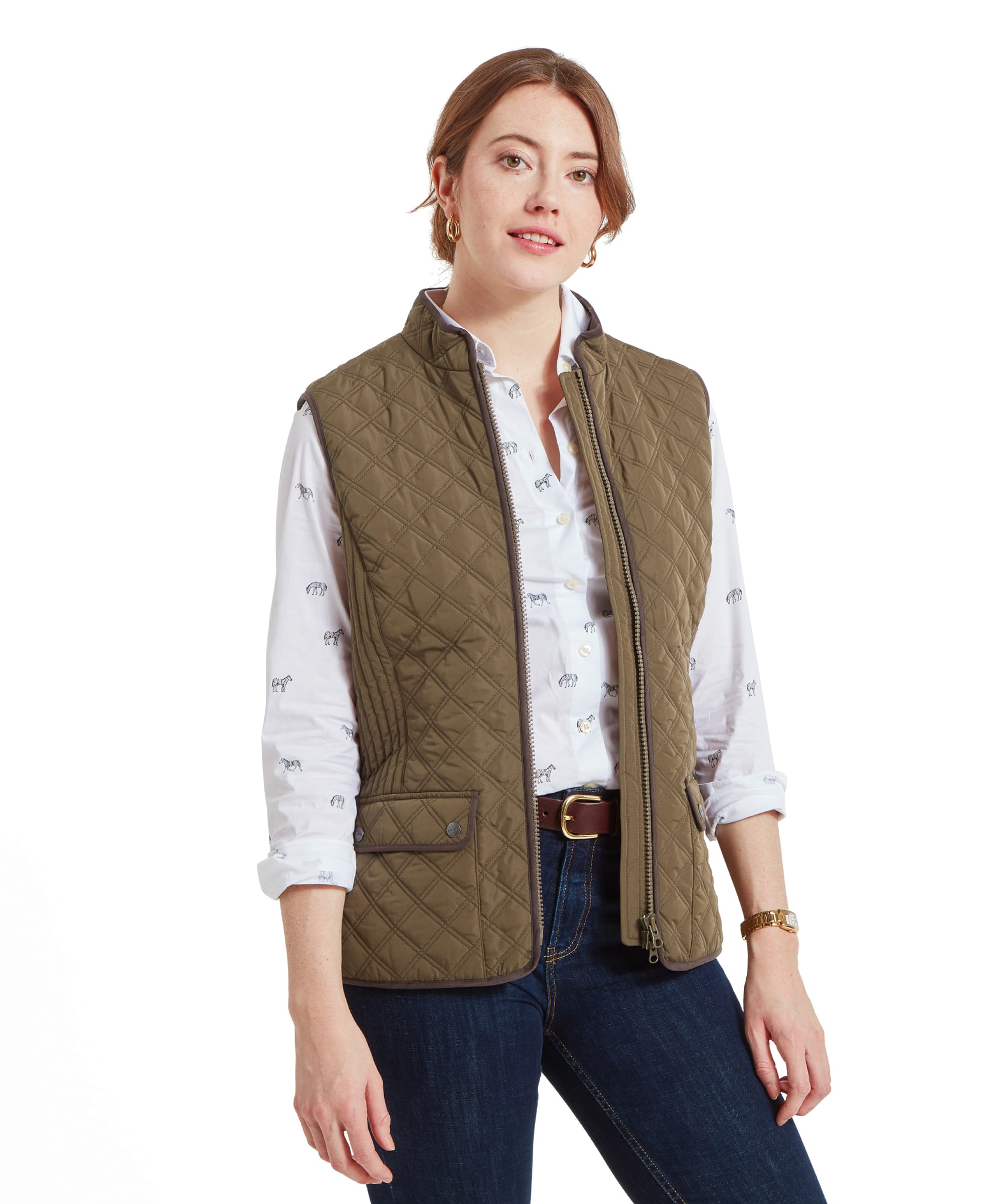 A woman wearing a Schöffel Quilt Gilet for Women in Green over a white shirt with a subtle pattern, standing in a relaxed pose with her arms by her side.