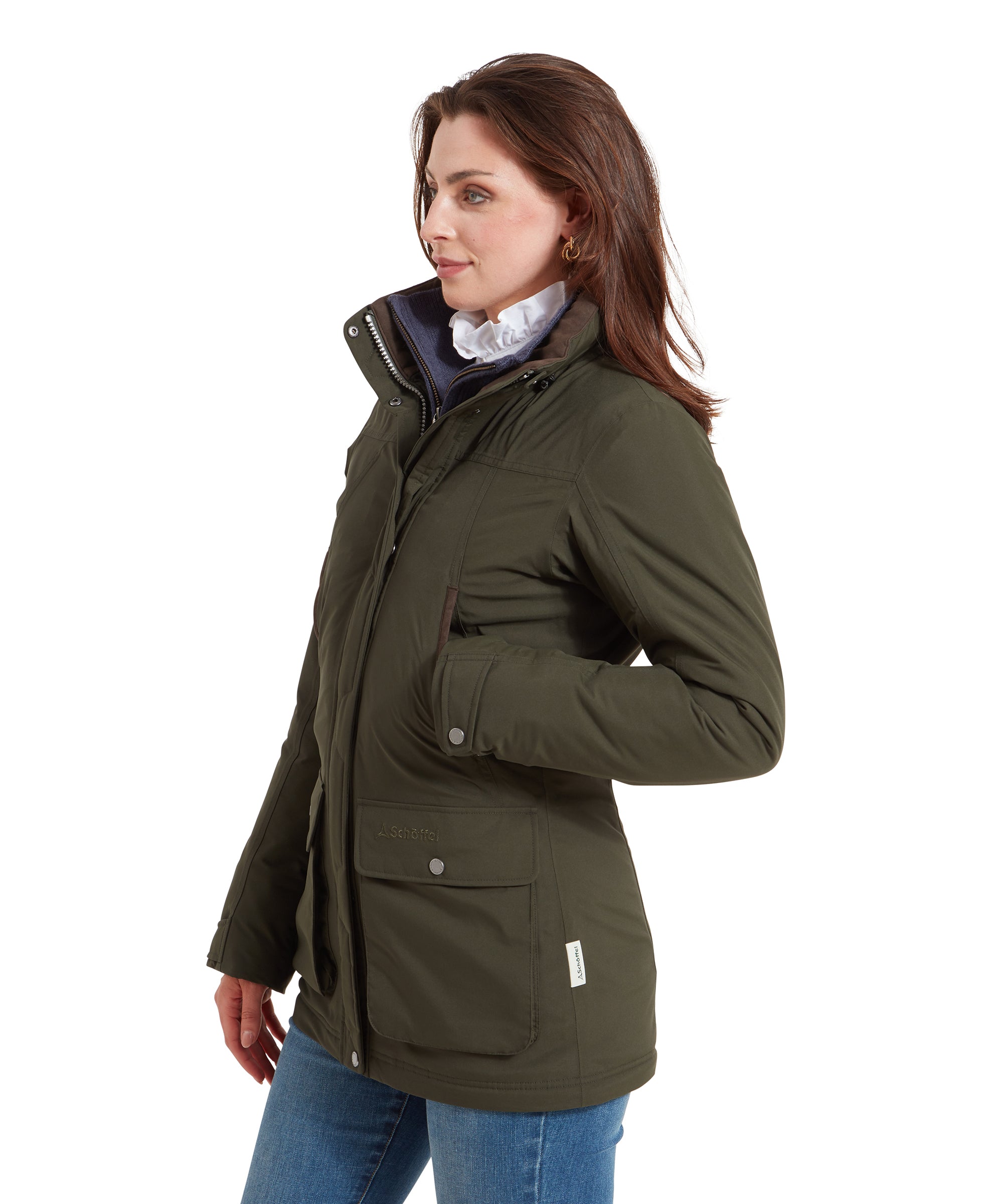 Side profile of the woman wearing the Schöffel Rockingham II Coat for Women in Green, showing the high collar and brown boots. She has her hands in the pockets.