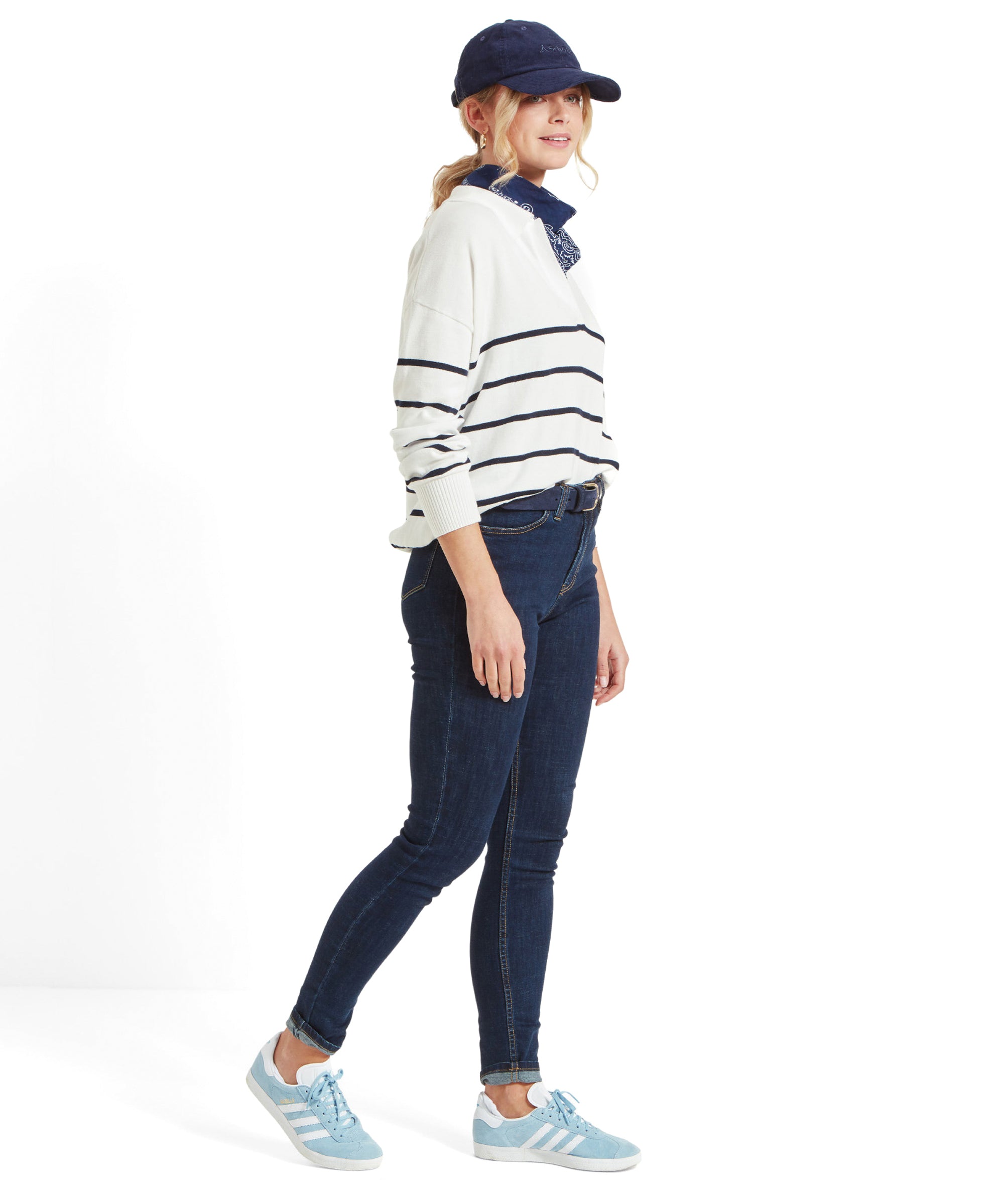 A woman wearing a Schöffel Roseland Jumper for Women in Navy, dark blue jeans, light blue trainers, a navy blue cap, and a navy blue bandana around her neck, standing sideways.