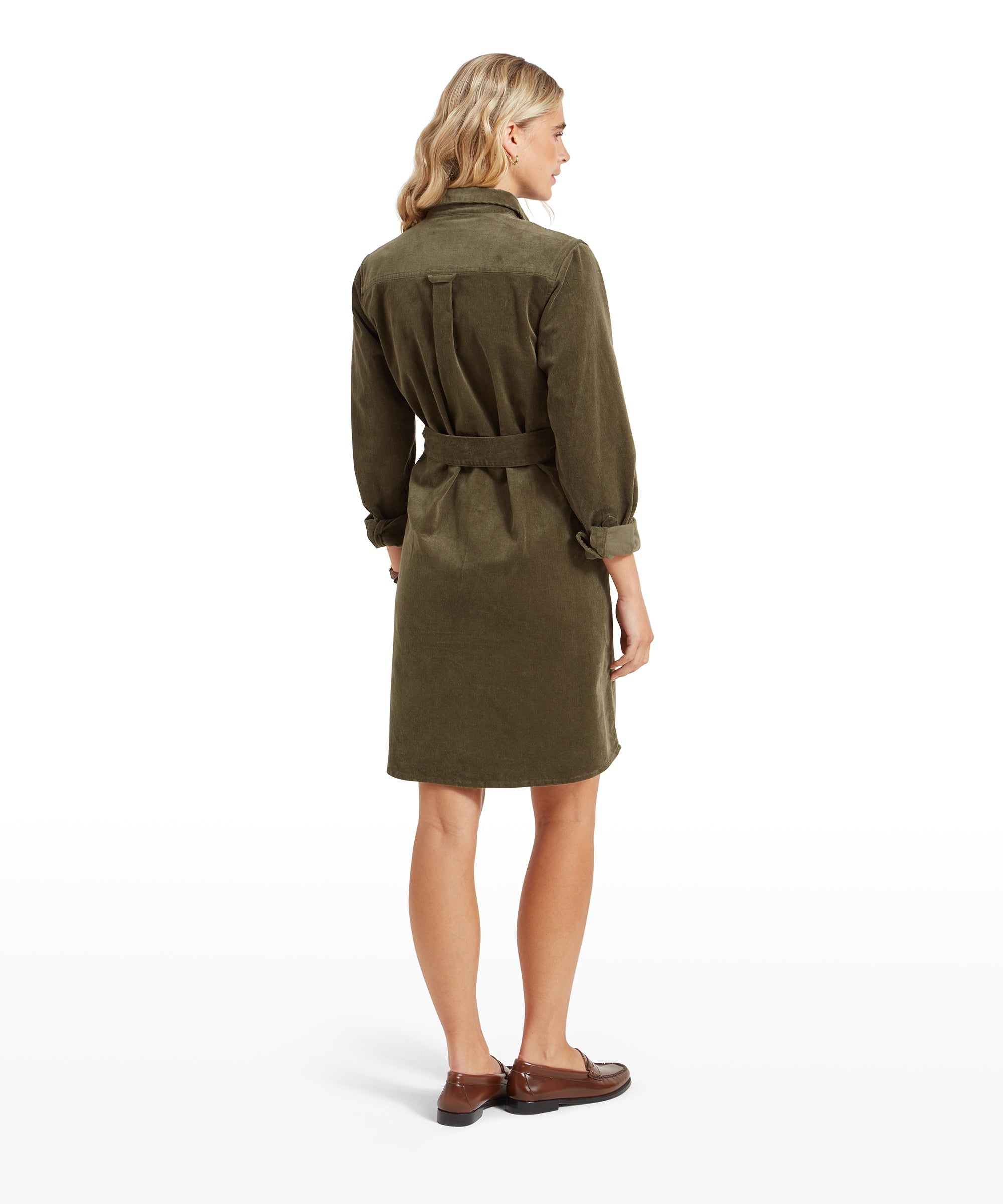 Rear view of the woman in the Schöffel Sage Cord Dress for Womens in Green, showing the back details of the dress, including the belt and pleats. Her arms are slightly relaxed by her sides.