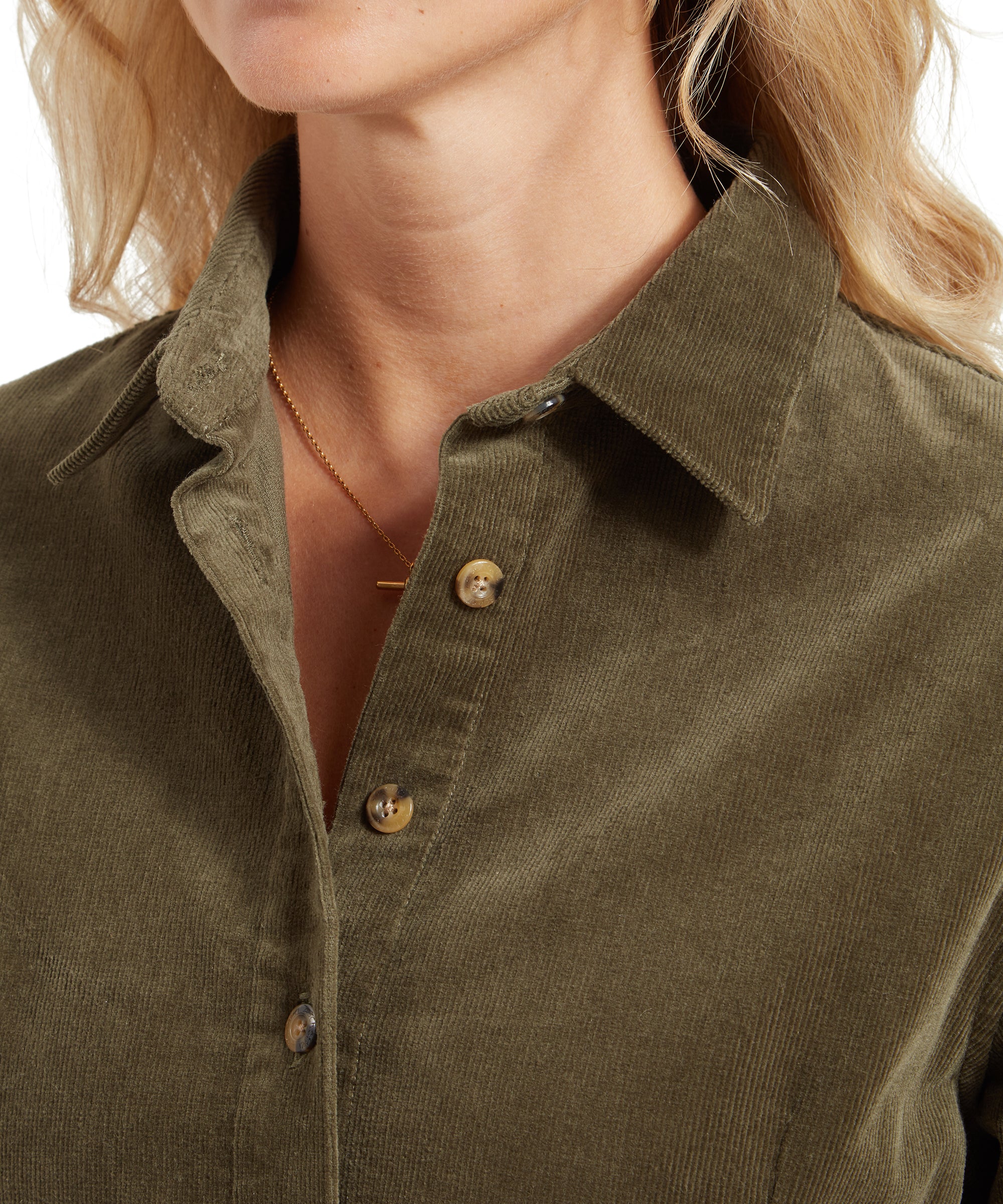 Close-up of the Schöffel Sage Cord Dress for Womens in Green's collar, showing the texture of the fabric and the buttons. The woman's blonde hair cascades down her shoulder, and she is wearing a simple necklace.