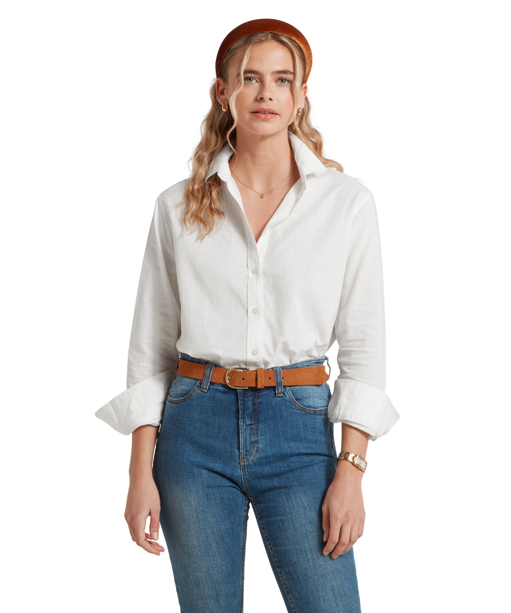 Close-up of a female model wearing a tucked in white linen Schöffel shirt, paired with mid denim jeans and tan leather belt. She is standing in a relaxed pose with her hands by her side.