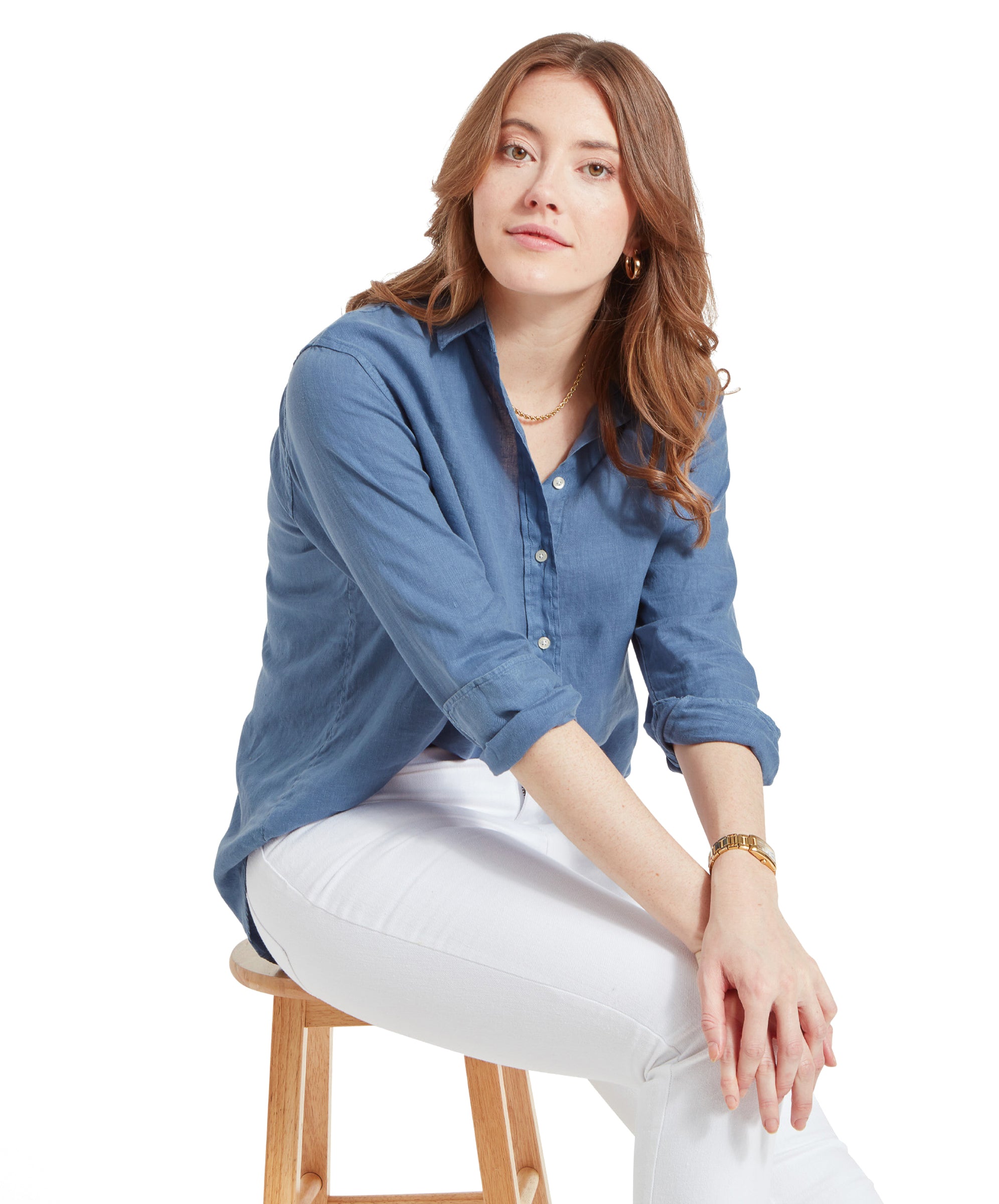 Woman seated on a stool, wearing a Schöffel Salthouse Linen Shirt for Women in Blue, white jeans, and a gold wristwatch.