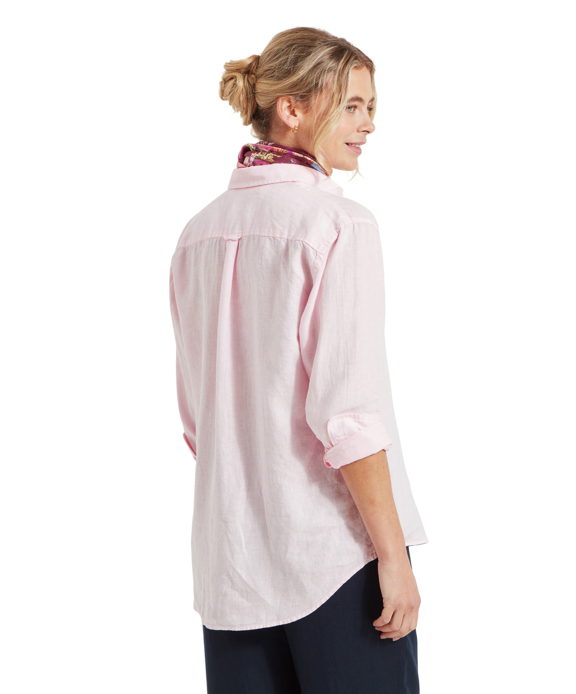 A side profile of the woman shows her looking over her shoulder. The Schöffel Salthouse Linen Shirt for Women in Pink is seen from the back, showing its relaxed, slightly oversized fit. Her hair is pulled back into a loose bun.