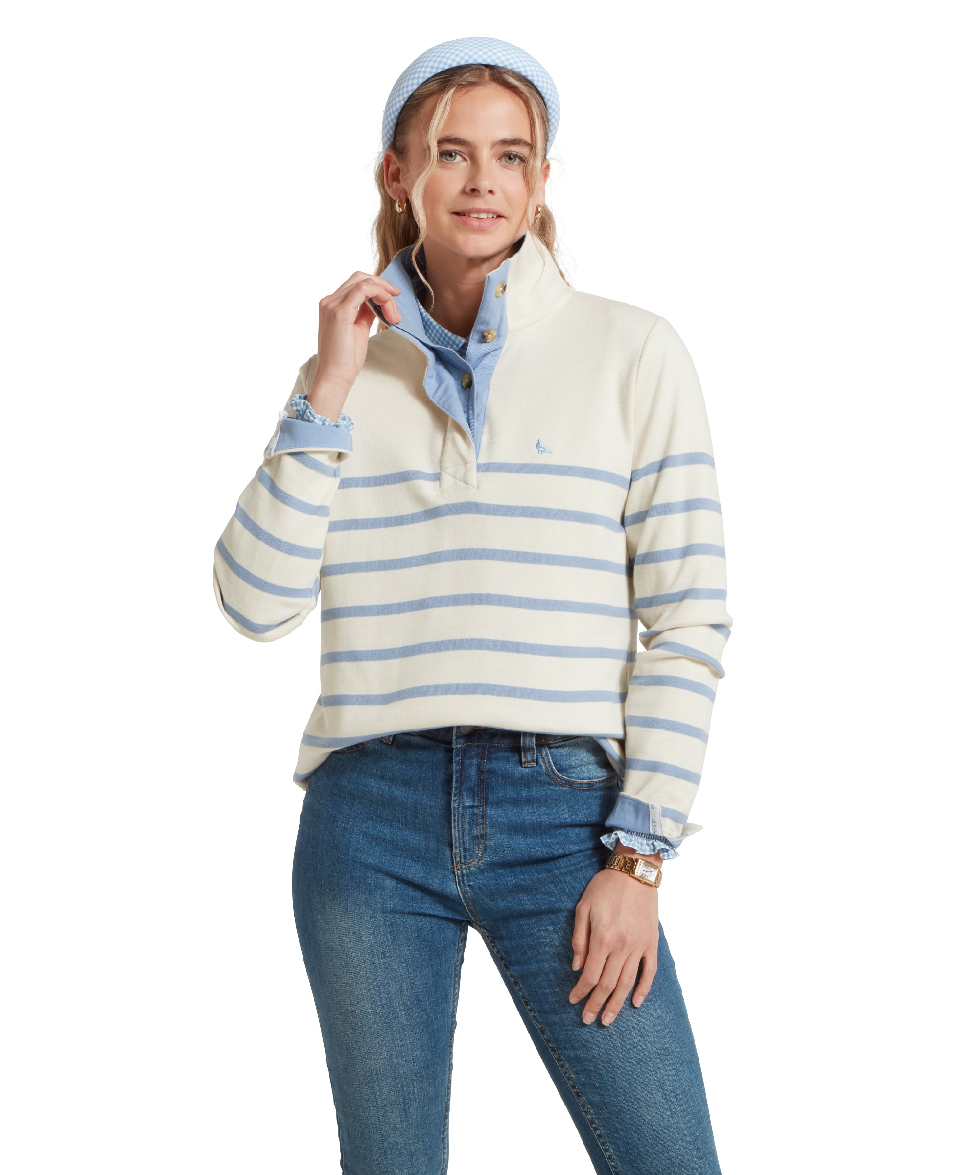 Female model standing in a relaxed pose, wearing a beige and blue striped Schöffel sweatshirt with a small embroidered bird logo on the chest, blue shirt and denim blue jeans.