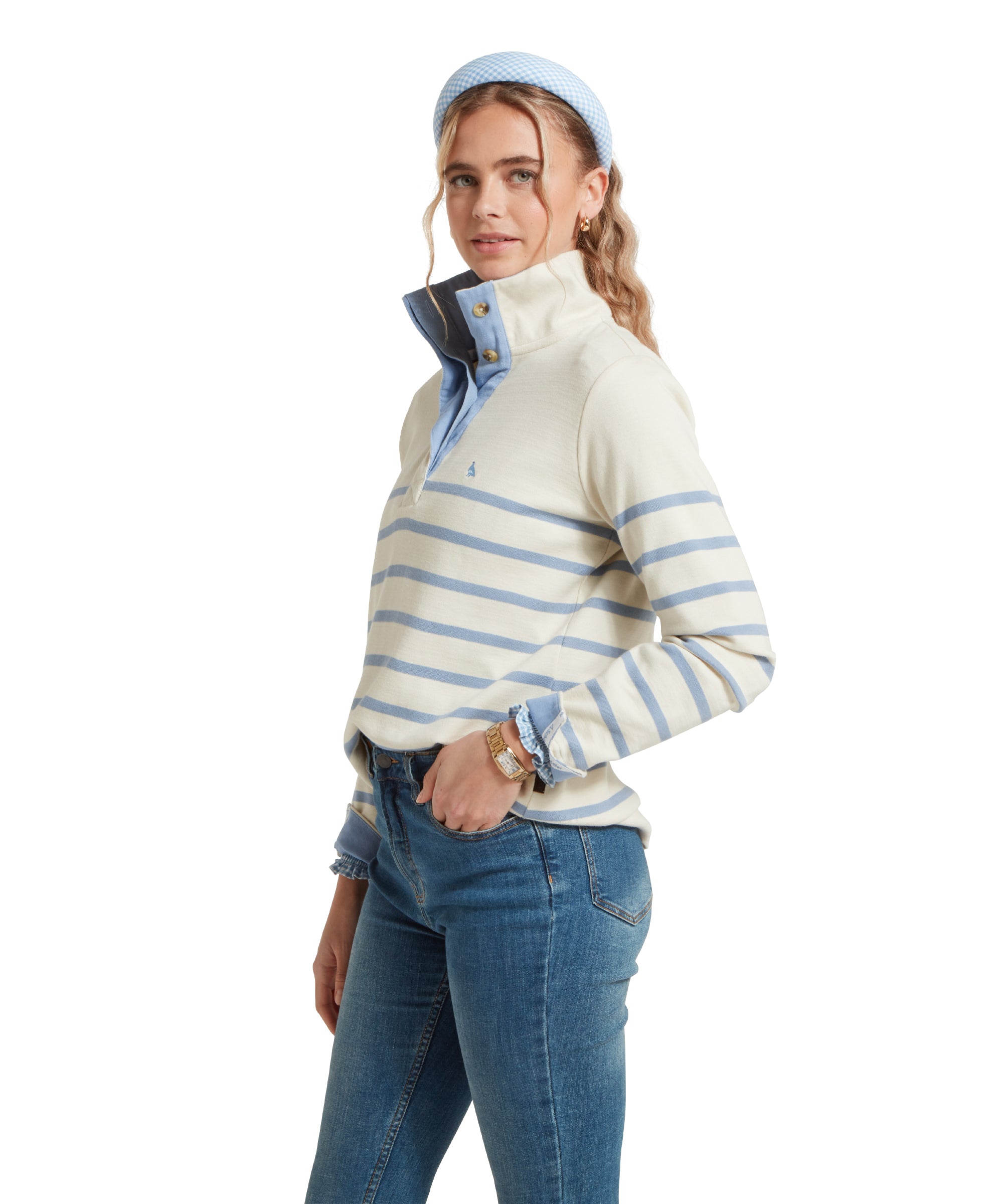 Female model standing sideways with hands in pockets, wearing a beige and blue striped Schöffel sweatshirt with a small embroidered bird logo on the chest, blue shirt, denim blue jeans.