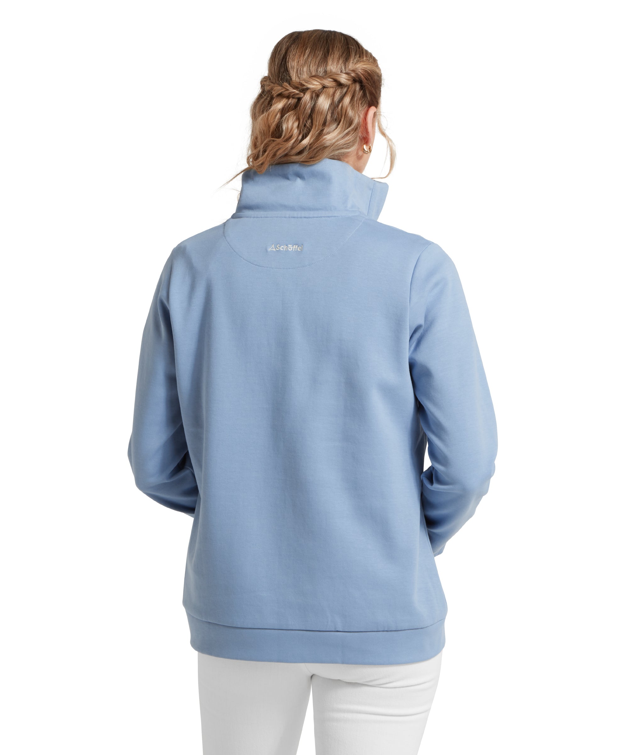 Rear view of a female model wearing a blue Schöffel sweatshirt with a small 'Schöffel' logo on the back, paired with white jeans.