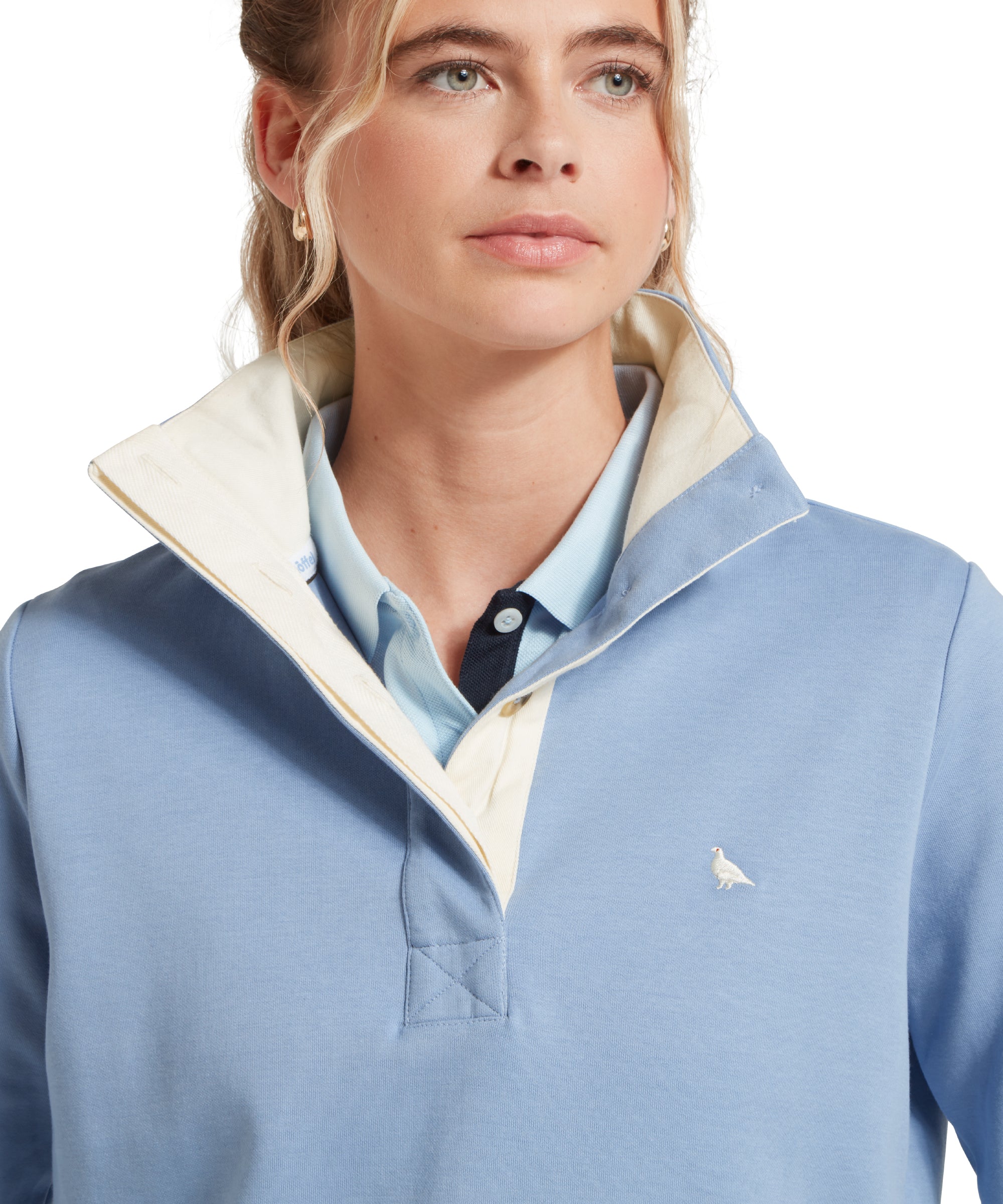 Close-up of a female model wearing a light blue Schöffel sweatshirt with a small embroidered bird logo on the chest, paired with a blue polo shirt.