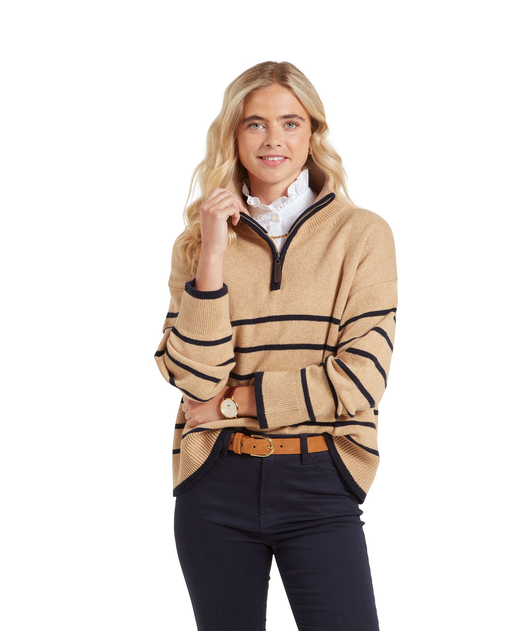 A woman wearing a Schöffel Sandsend 1/4 Jumper for Women in Beige, standing confidently with her hand near her chin. She pairs the jumper with navy trousers and a tan belt, smiling subtly.