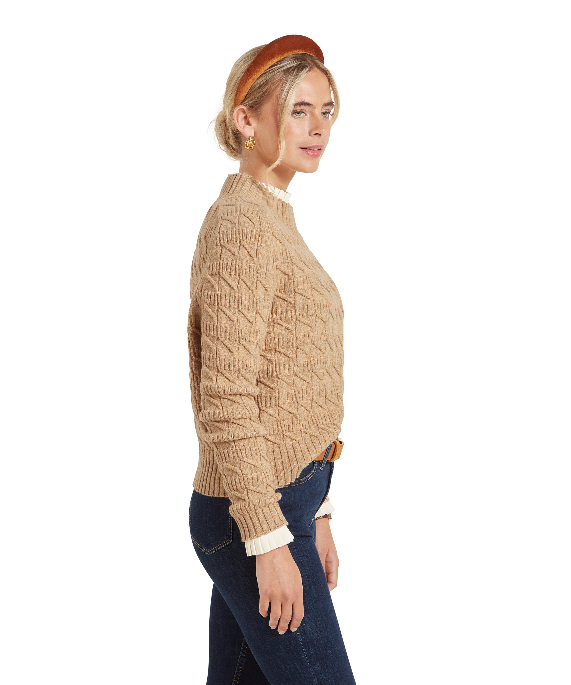 Side view of a woman wearing a Schöffel Sandsend Cable Jumper for Women in Beige with a patterned hairband, dark blue jeans and create top.