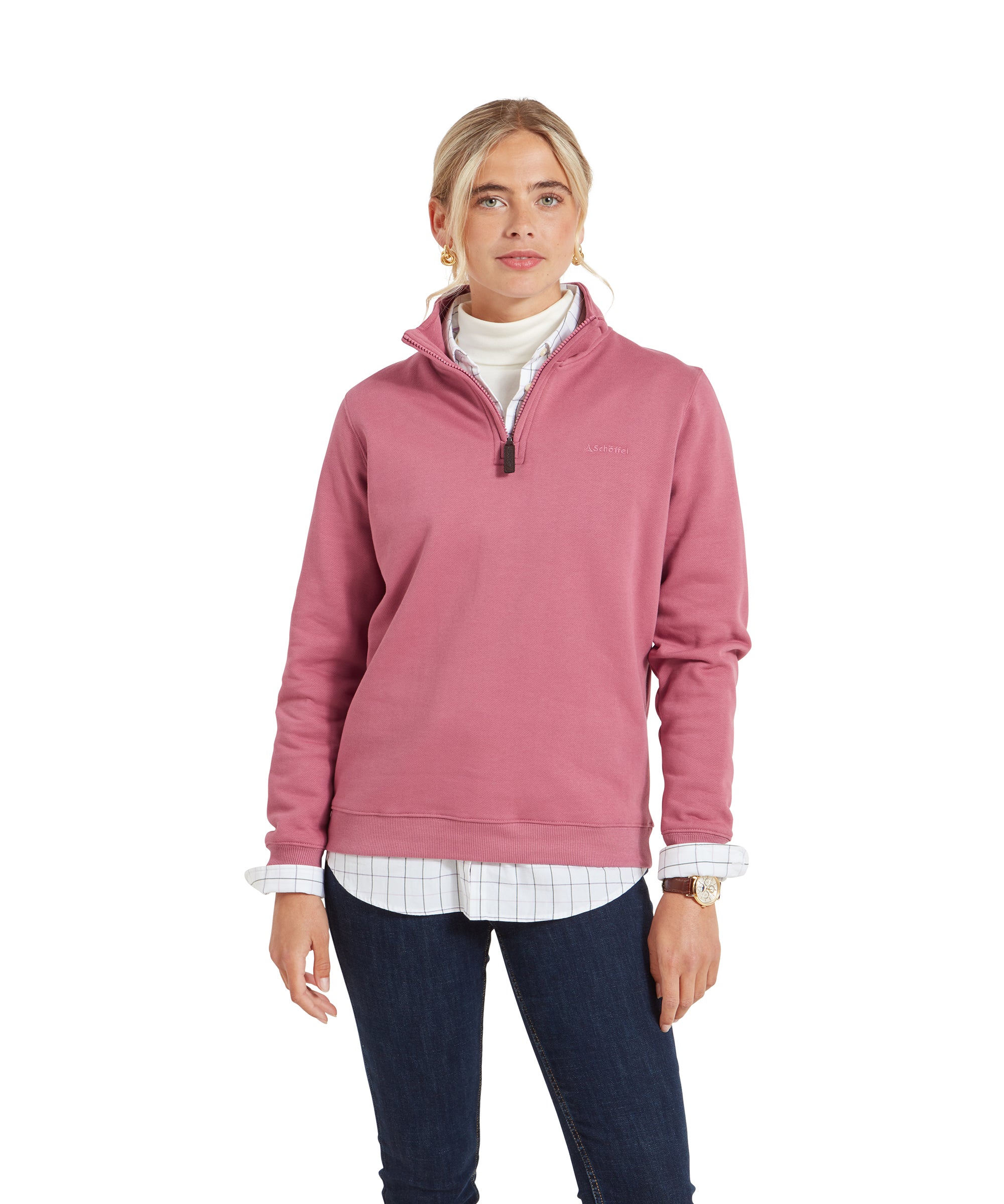 A woman wearing a Schöffel Sennen Cove Sweatshirt for Womens in Pink, layered over a white turtleneck and checkered shirt, standing with her hands relaxed by her sides.