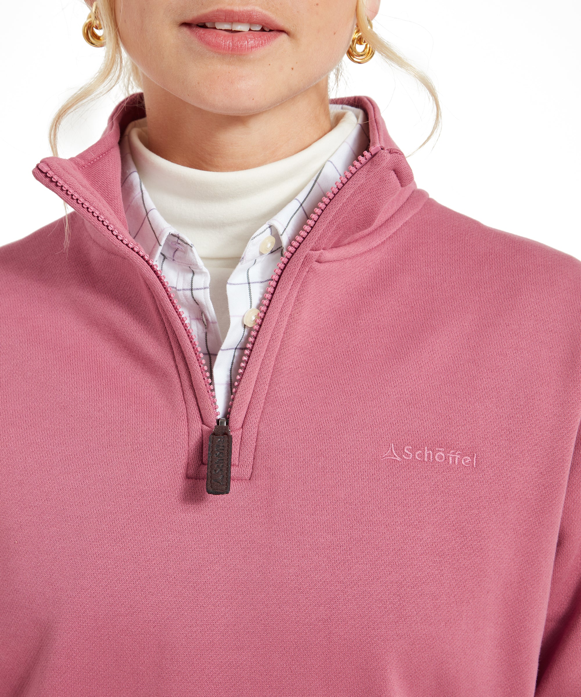 Close-up of the front zip detail of the Schöffel Sennen Cove Sweatshirt for Womens in Pink, featuring the logo and layered turtleneck and checkered shirt underneath.