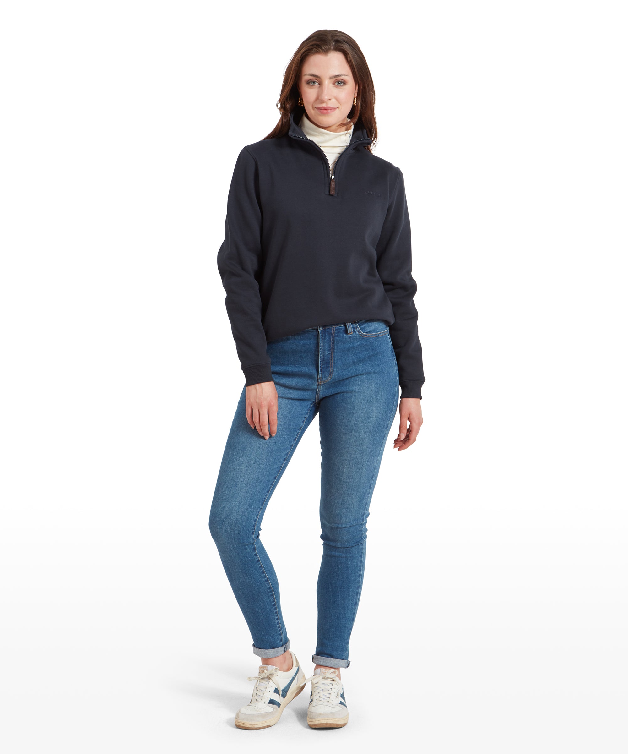 Full-body shot of a woman in a Schöffel Sennen Cove Sweatshirt for Womens in Dark Blue, blue jeans, and white trainers, posing casually.