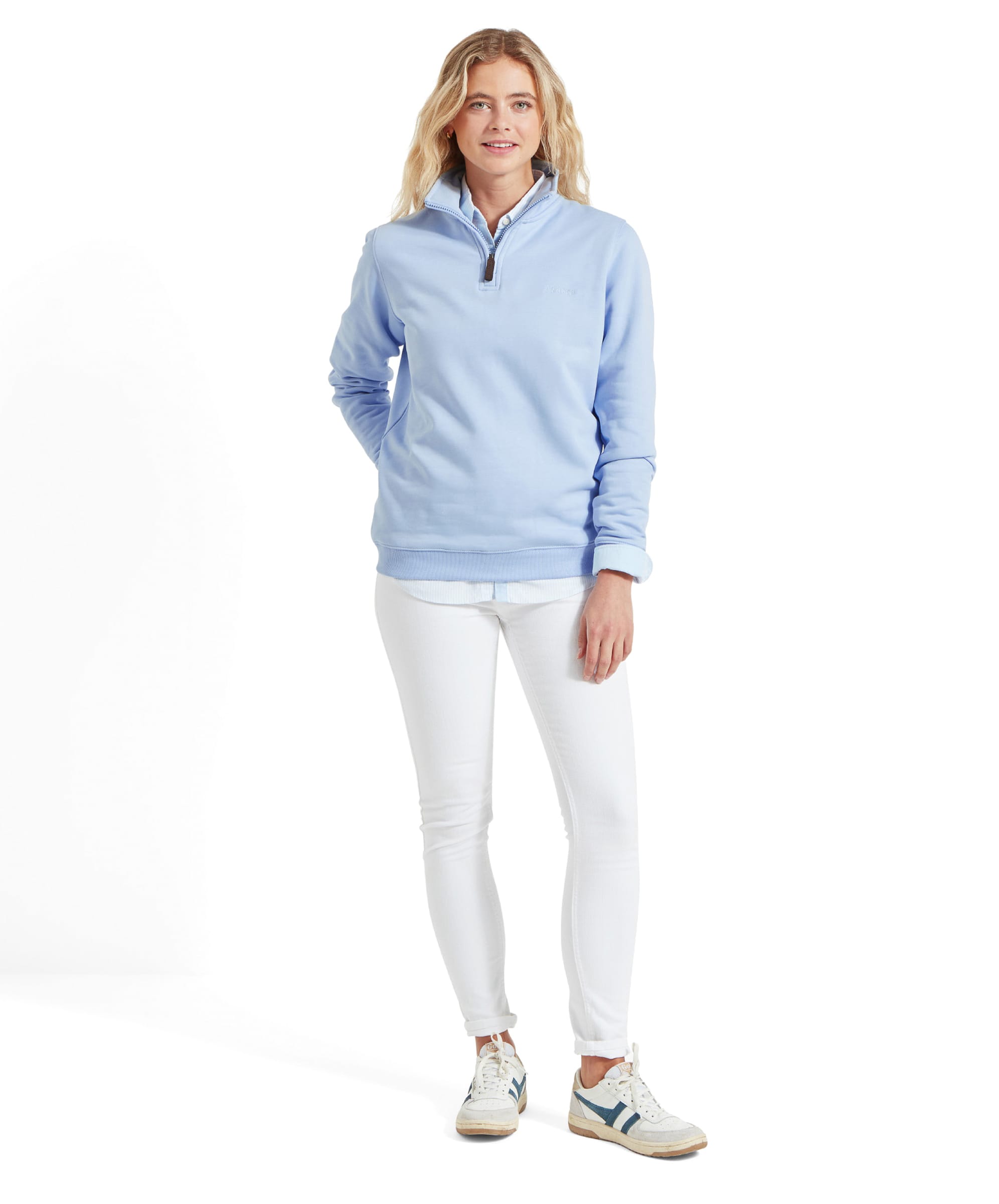 Full-body front view of the woman standing in the Schöffel Sennen Cove Sweatshirt for Womens in Blue, white jeans, and white trainers with blue accents, posing with a relaxed smile.