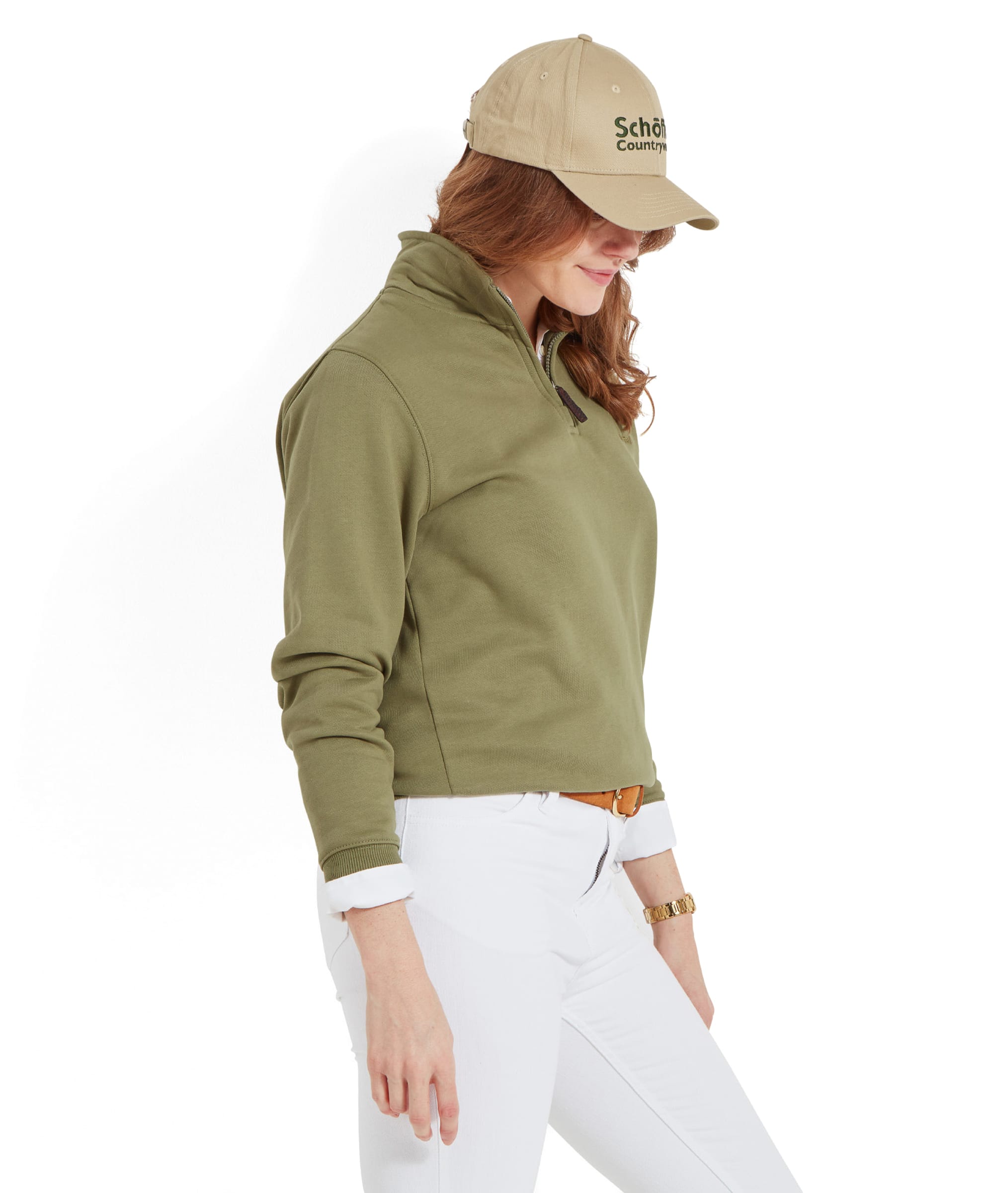 Side profile of a woman wearing a Schöffel Sennen Cove Sweatshirt for Womens in Green with a beige cap, looking down with hands resting on her sides.