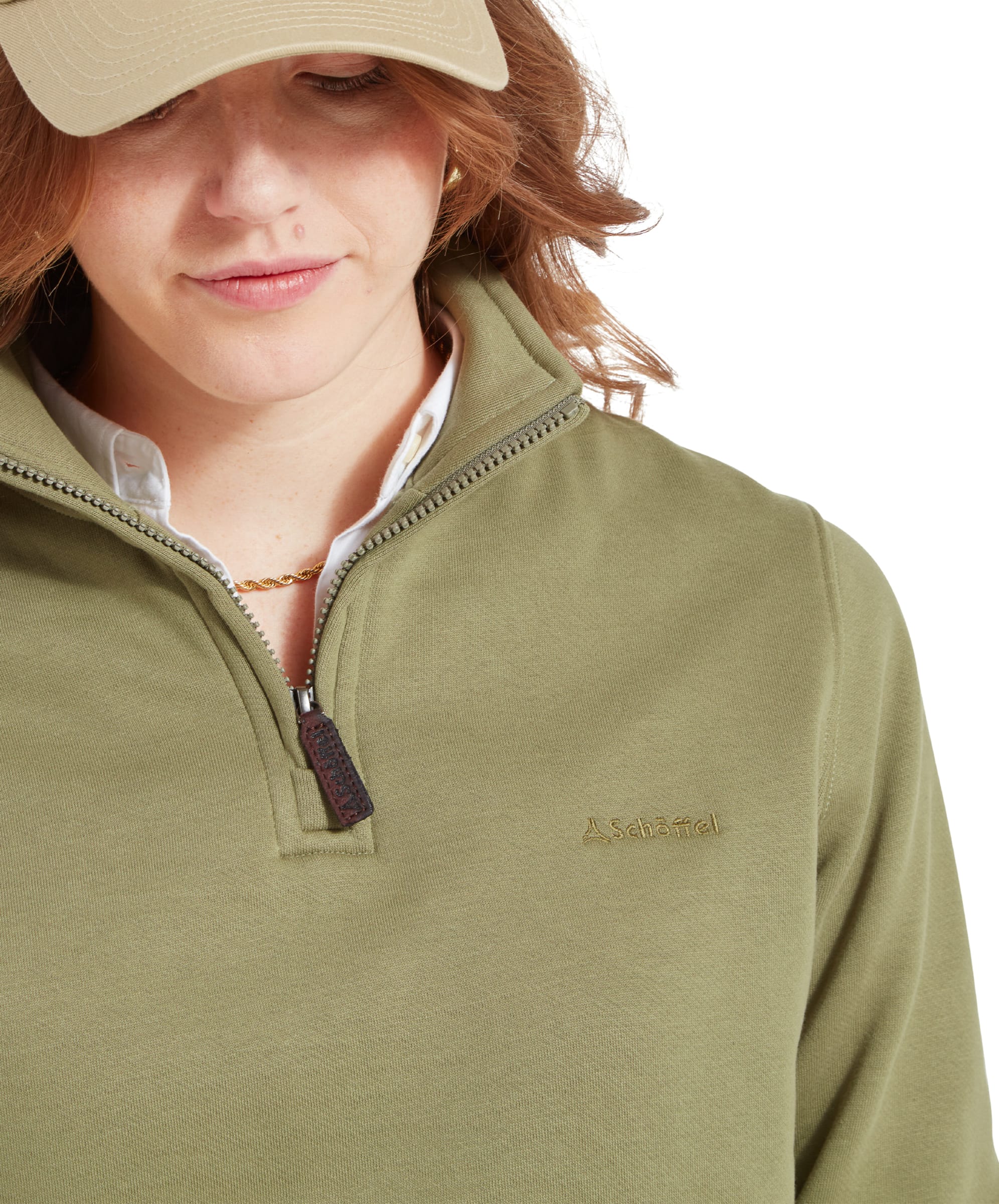 Close-up of the chest area of a Schöffel Sennen Cove Sweatshirt for Womens in Green, showing the embroidered logo and zipper detail, worn by a woman with a beige cap.