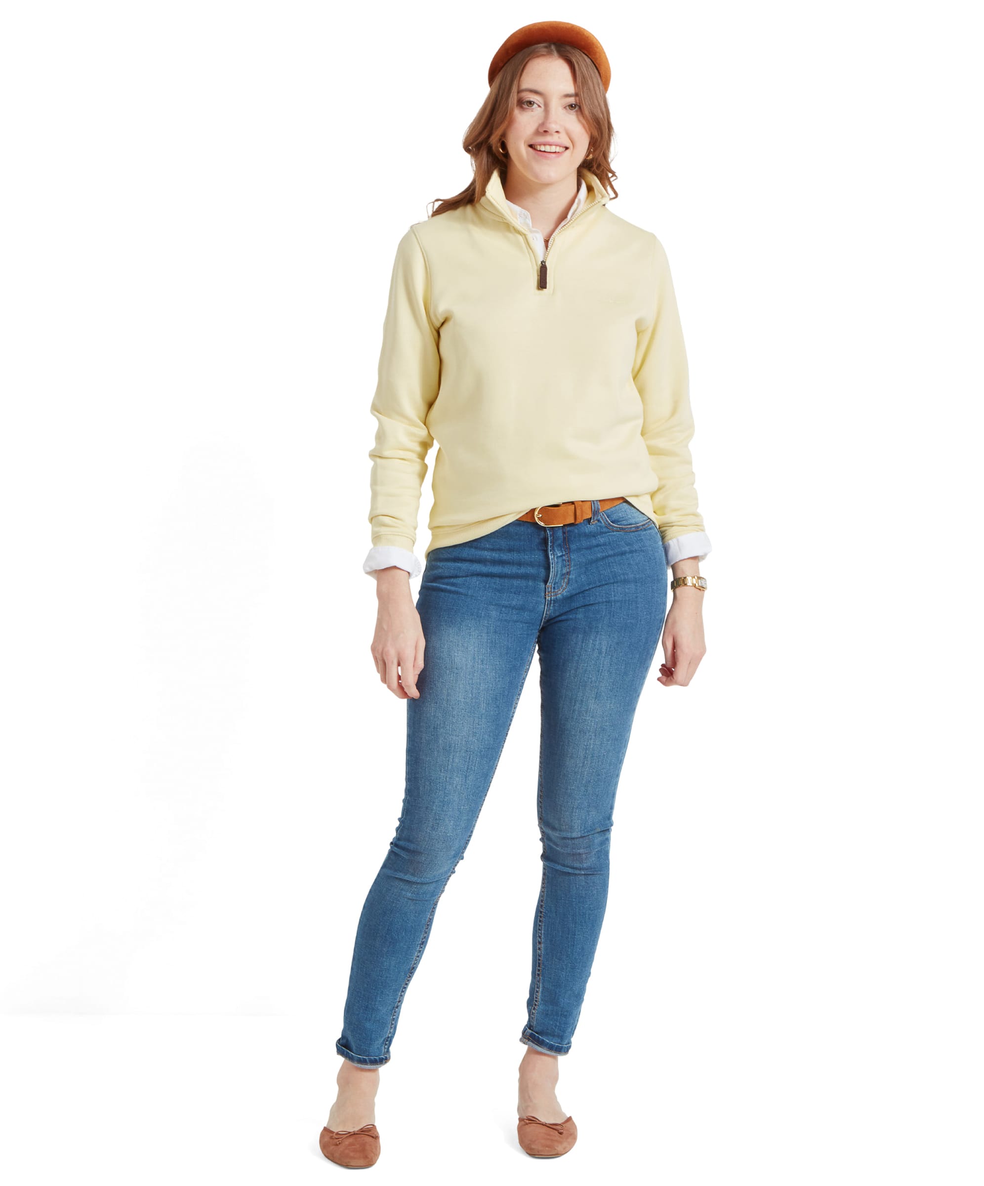 A full-body image of the woman in the Schöffel Sennen Cove Sweatshirt for Womens in Yellow. She is smiling and standing with one foot slightly forward. Her outfit includes blue jeans, brown flats, and a brown headband, creating a coordinated and casual ensemble.