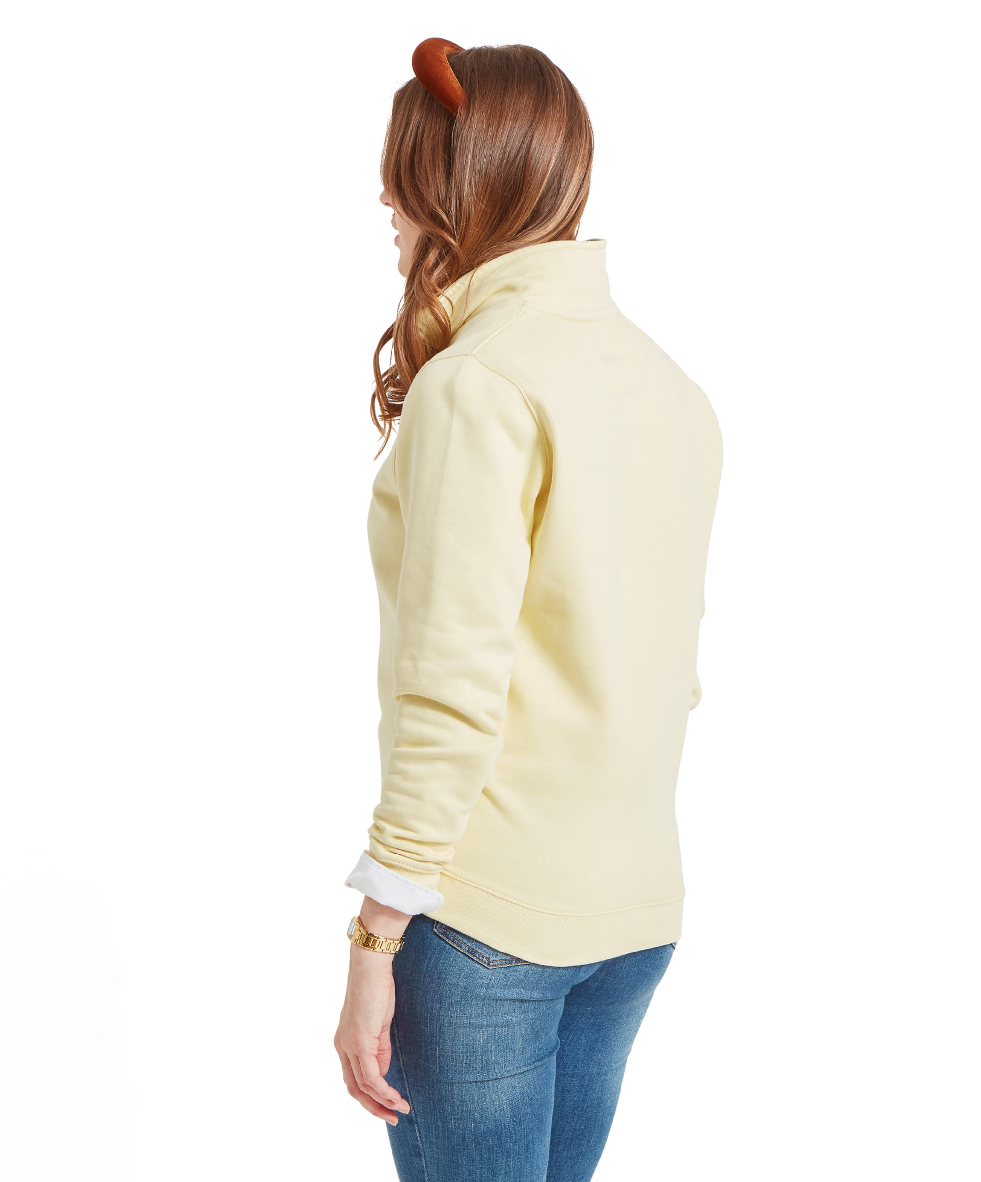 A back view of the woman in the Schöffel Sennen Cove Sweatshirt for Womens in Yellow. The sweatshirt’s collar is turned up slightly, and the woman’s hair is flowing freely. Her jeans fit snugly, showing a casual and comfortable look from behind.