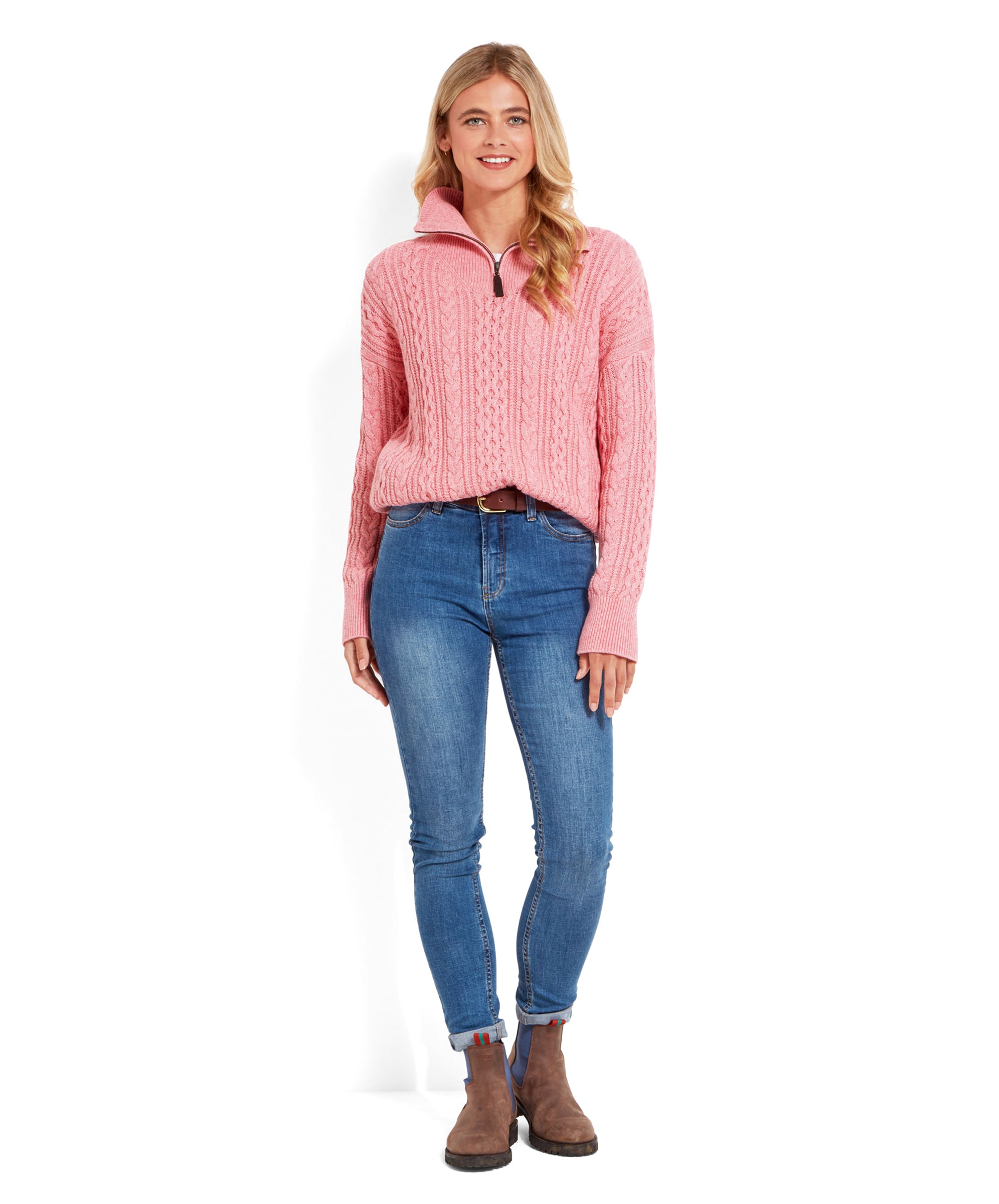 The same woman is shown in a full-body shot, wearing the Schöffel Settle 1/4 Zip for Women in Pink, blue jeans, and brown ankle boots. She is standing with a relaxed posture, her hands at her sides.