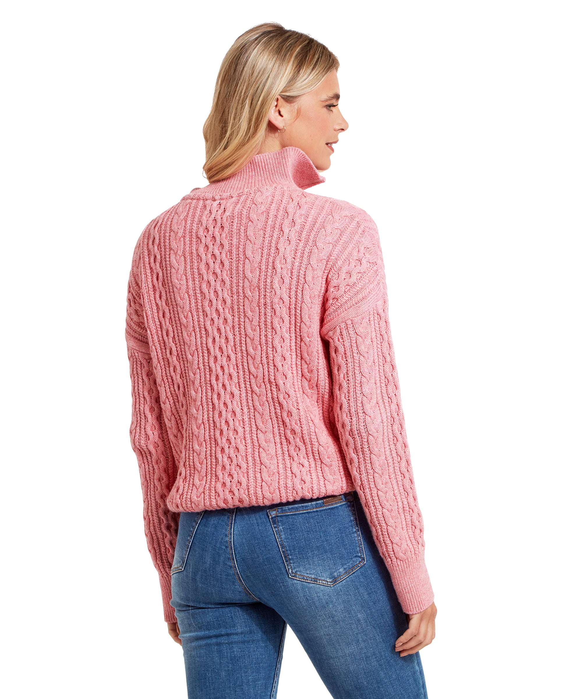 The woman is shown from the back, revealing the back design of the Schöffel Settle 1/4 Zip for Women in Pink. Her blonde hair is down, and she is wearing blue jeans that fit snugly, accentuating the sweater's relaxed fit.